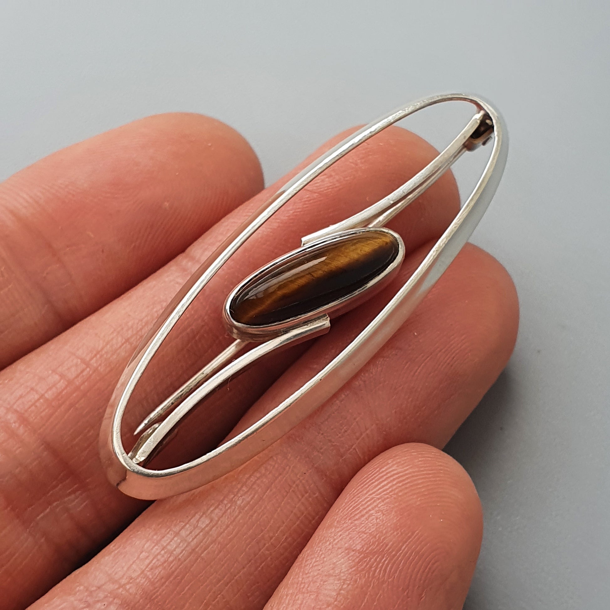 Elongated silver brooch or pendant with an oval brown gemstone in the center.