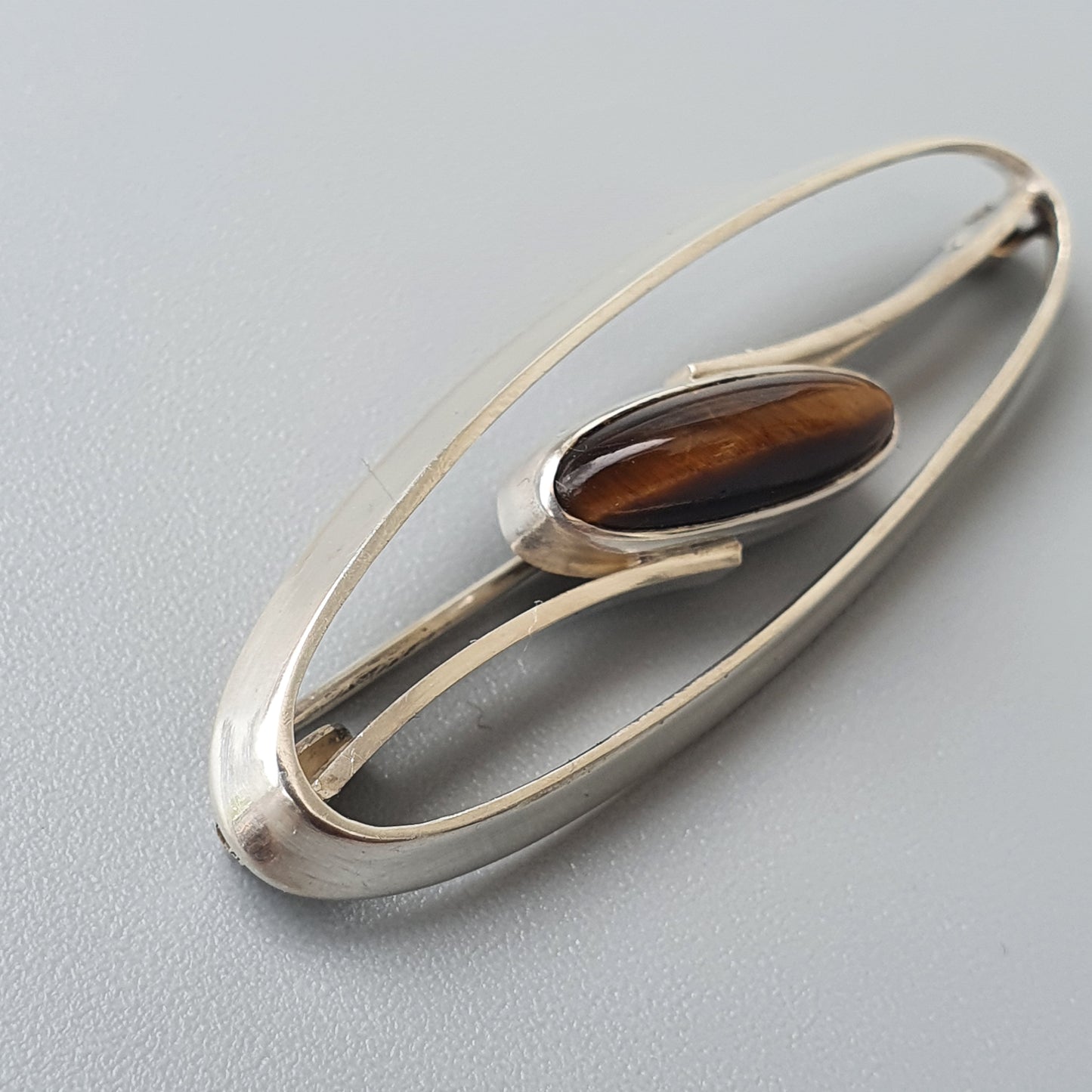 Elongated silver brooch with an oval brown gemstone set in the center.