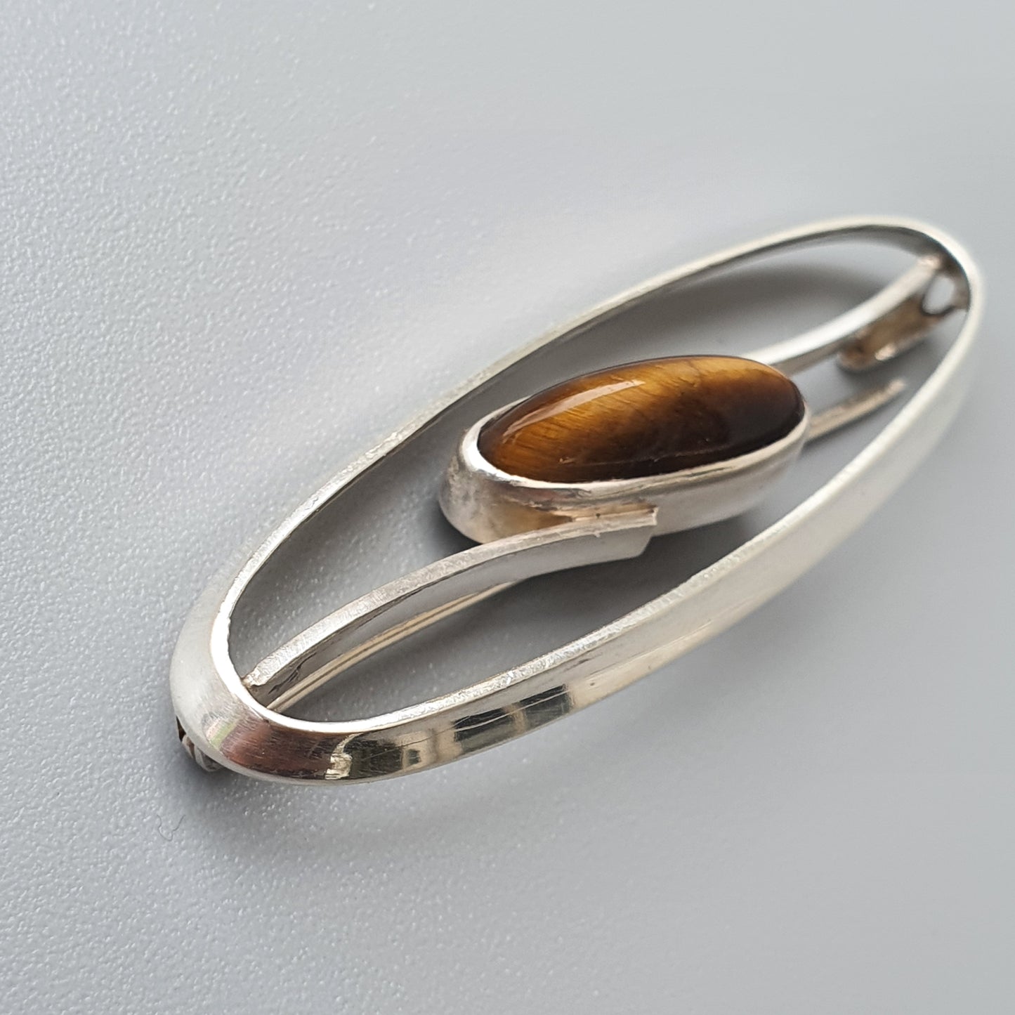 Sleek oval-shaped silver brooch with an amber-colored gemstone inset.