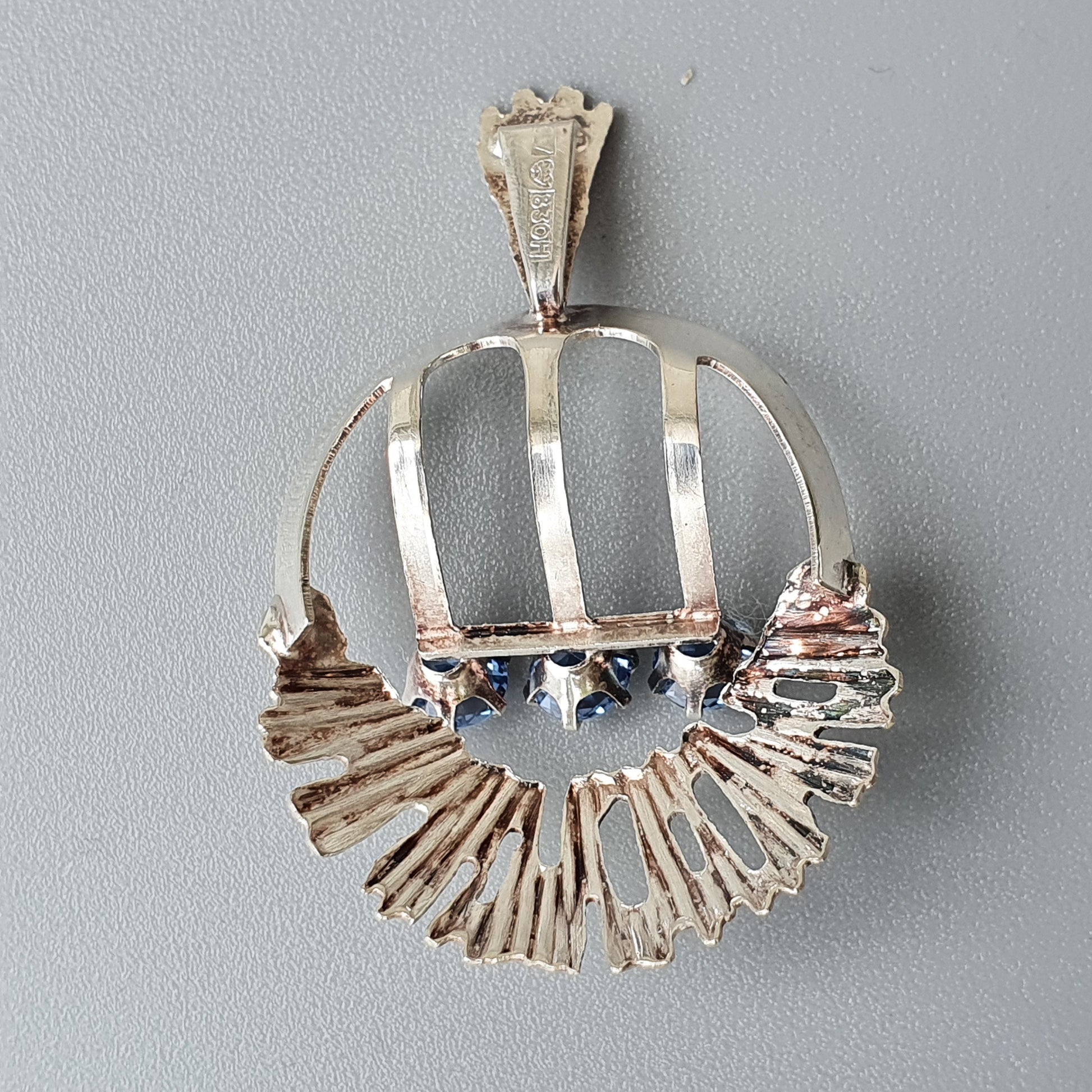 Silver pendant featuring a stylized crown design with radiating spokes at the bottom.