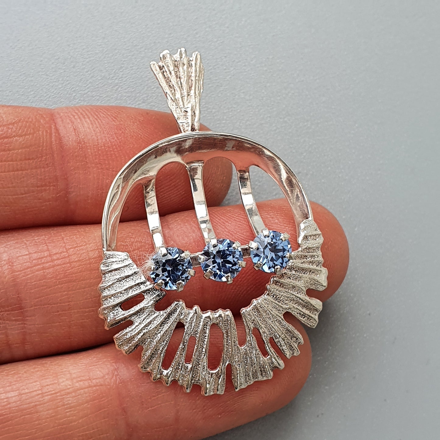 Silver pendant featuring a circular design with three blue gemstones.