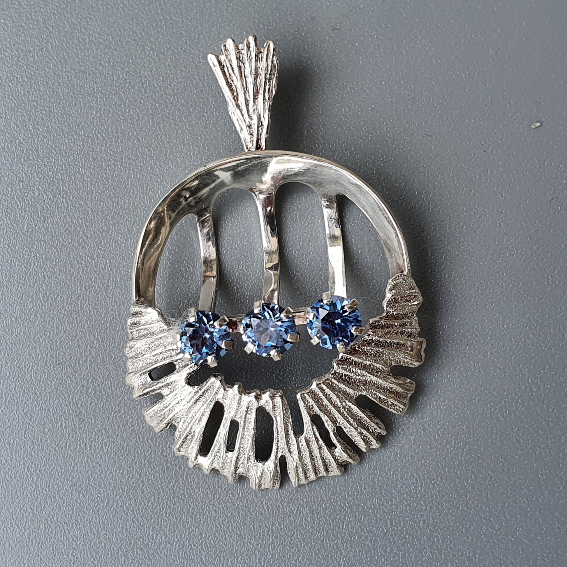 Silver pendant with a textured circular design and blue gemstones.