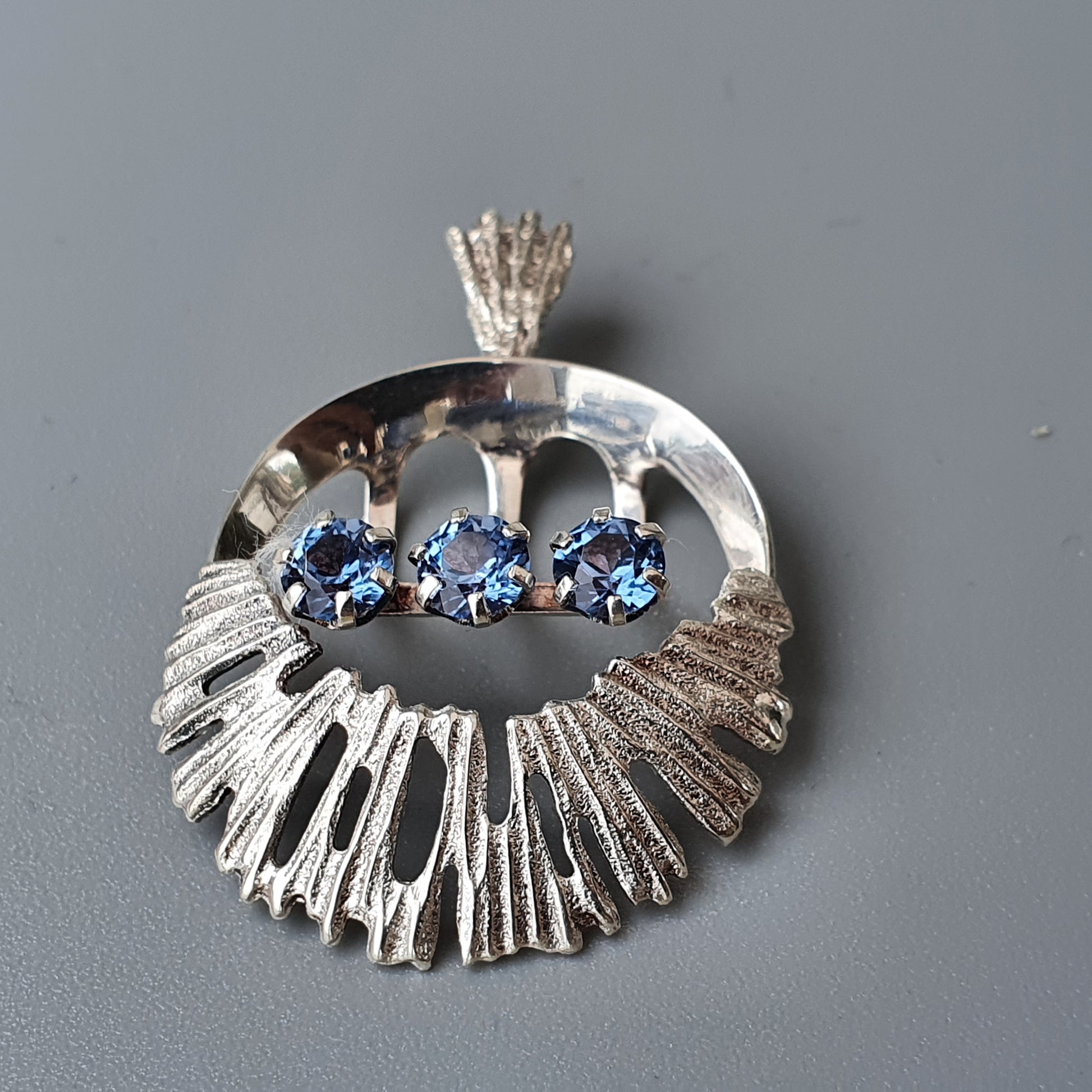 Silver pendant with a textured circular design and three blue gemstones.