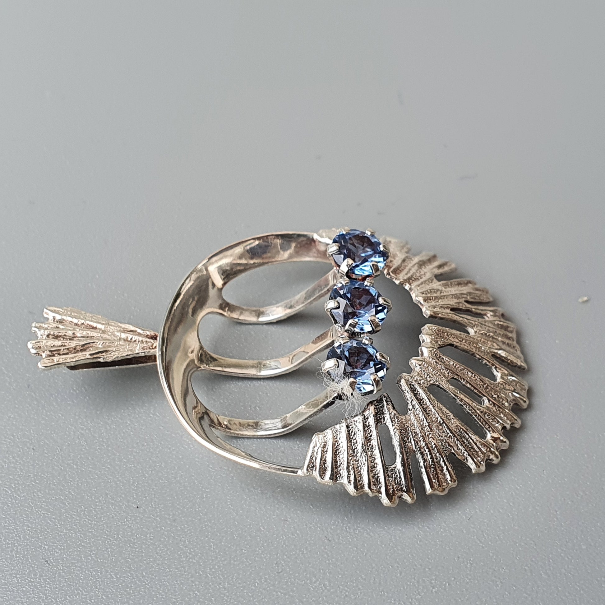 Silver brooch with a fan-like design featuring blue gemstones.