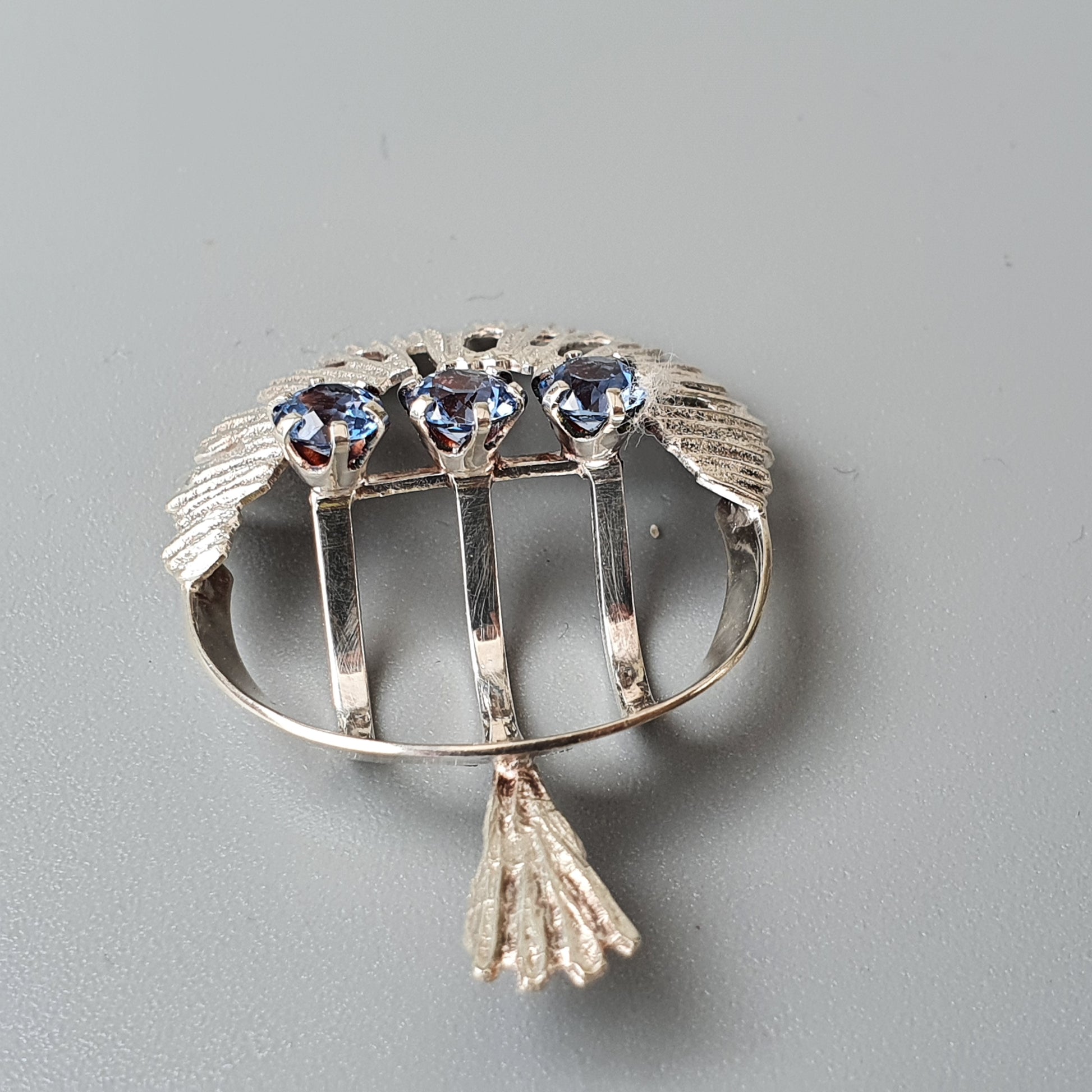 Silver brooch with three blue stones and wing-like designs.