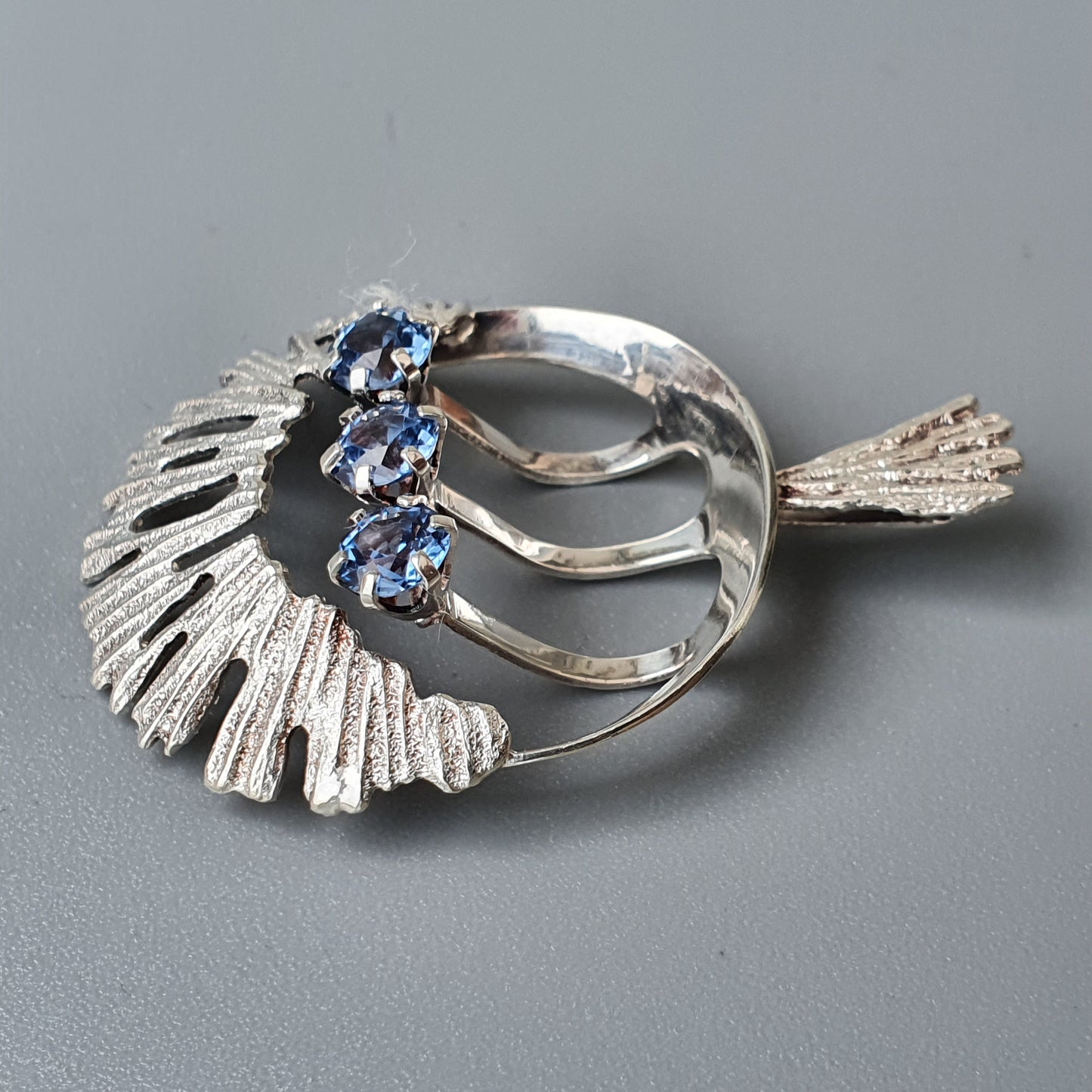 Vintage silver brooch with blue gemstones in a stylized leaf or feather design.