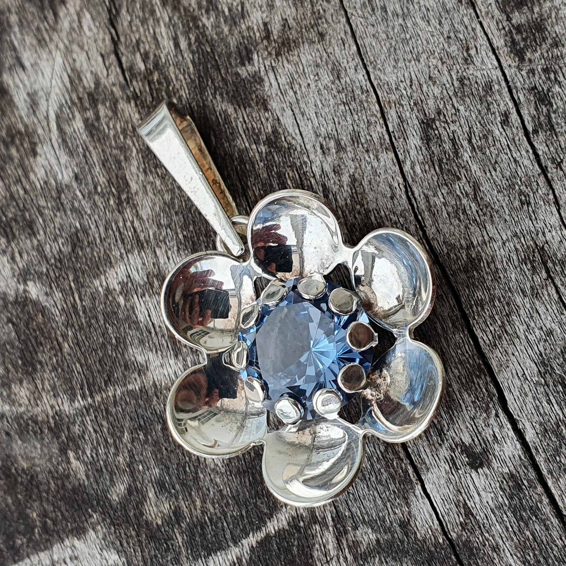 Silver flower-shaped pendant with a blue gemstone center.