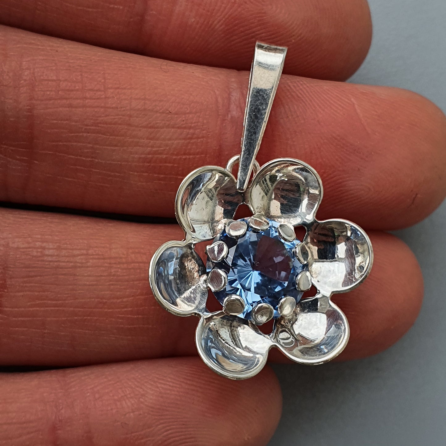 Silver flower-shaped pendant with a blue gemstone center.