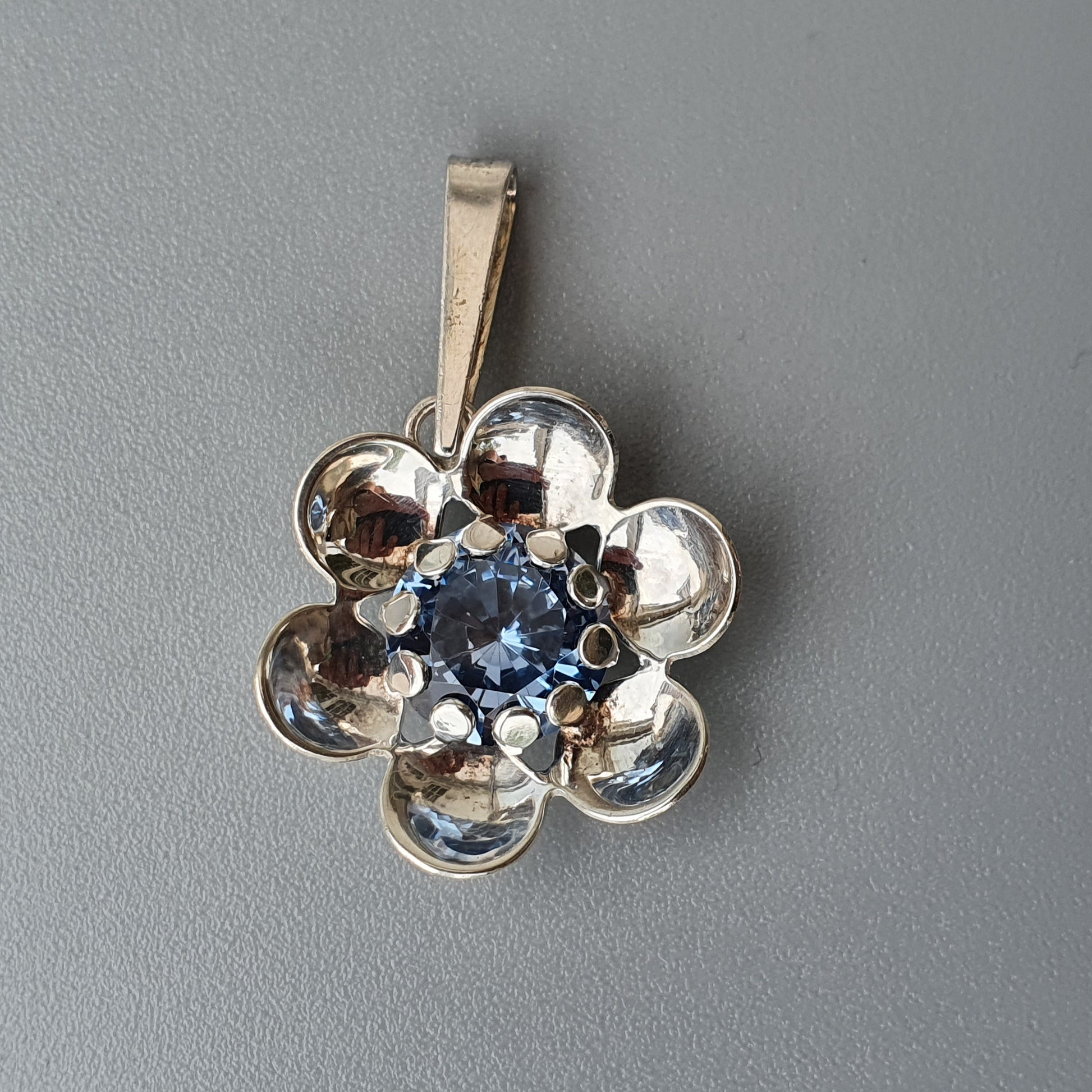 Silver flower-shaped pendant with a blue gemstone center.