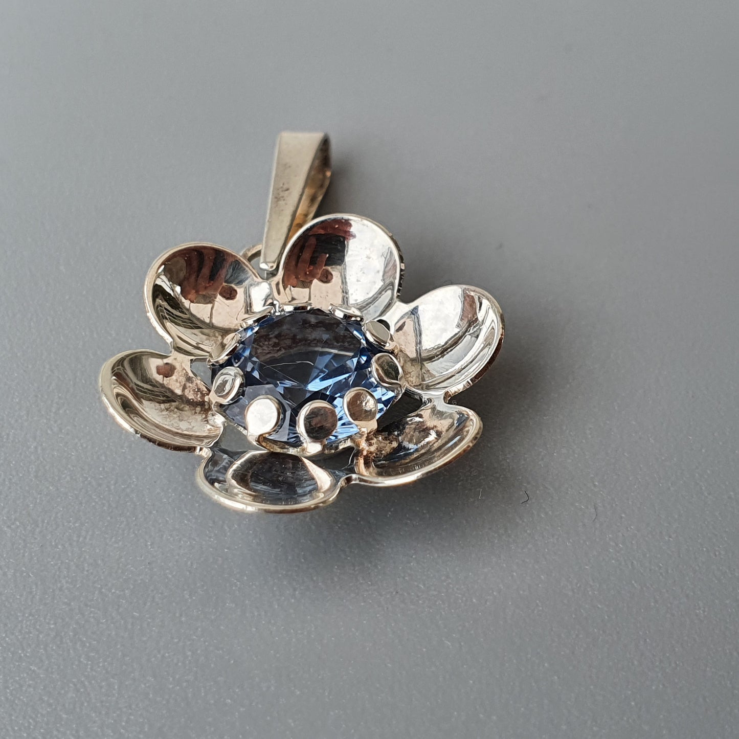 Silver flower-shaped pendant with blue gemstones in the center.