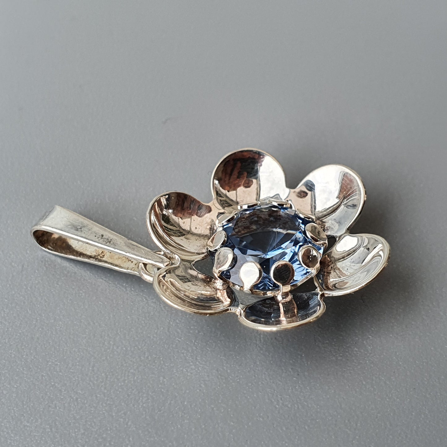 Silver flower-shaped pendant with a blue gemstone center.