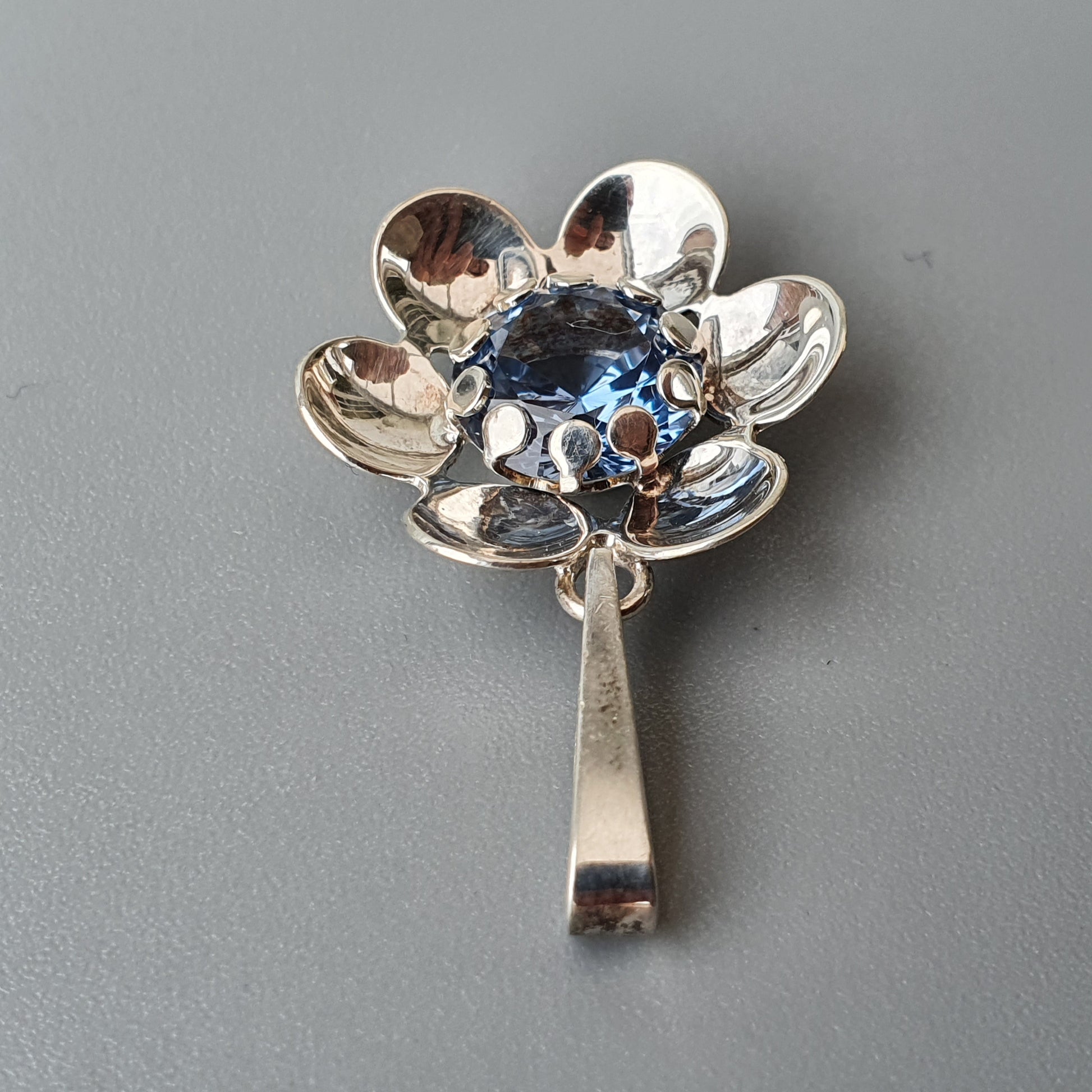 Silver flower-shaped brooch or pendant with a blue gemstone center.