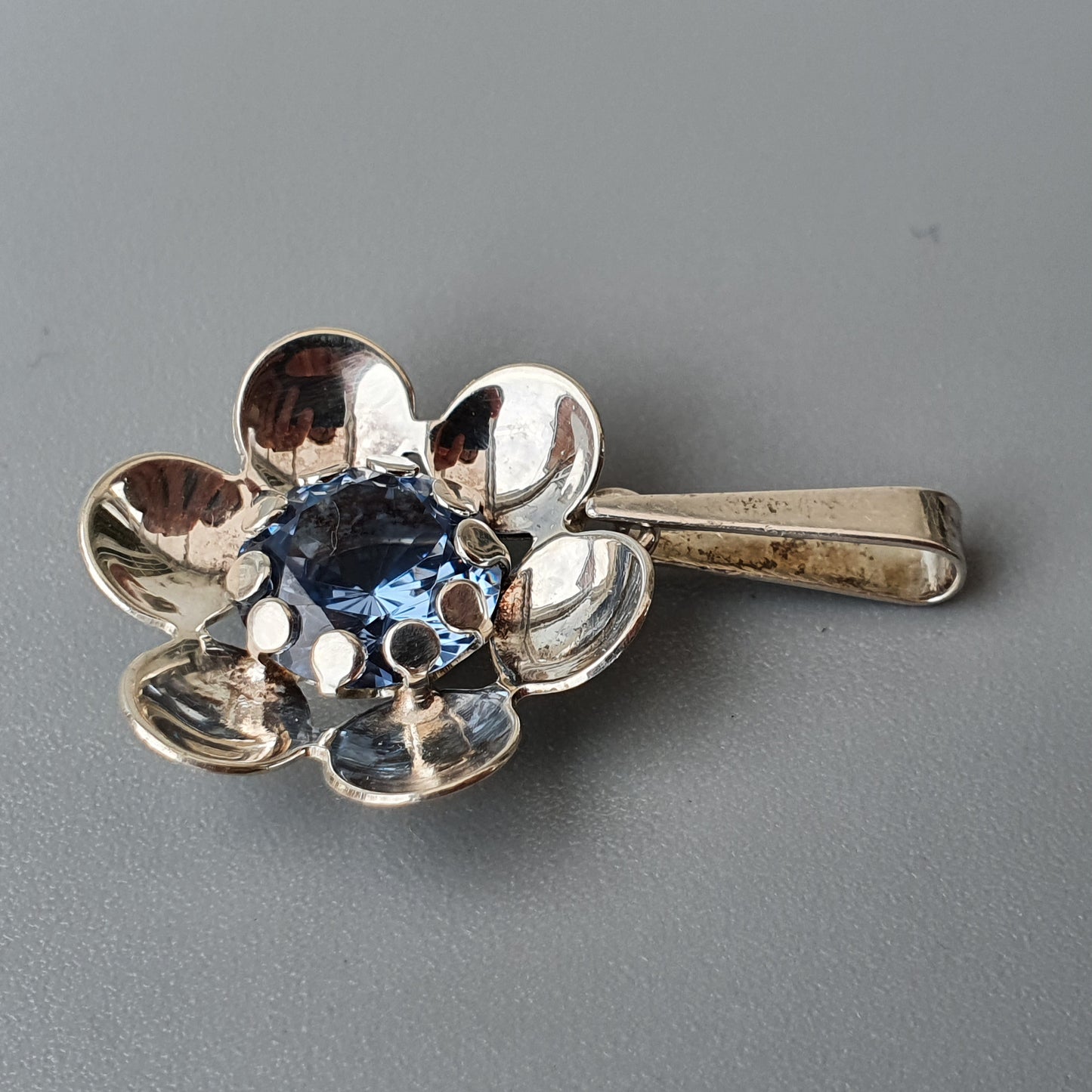 Silver flower-shaped brooch or hair clip with a blue gemstone center.