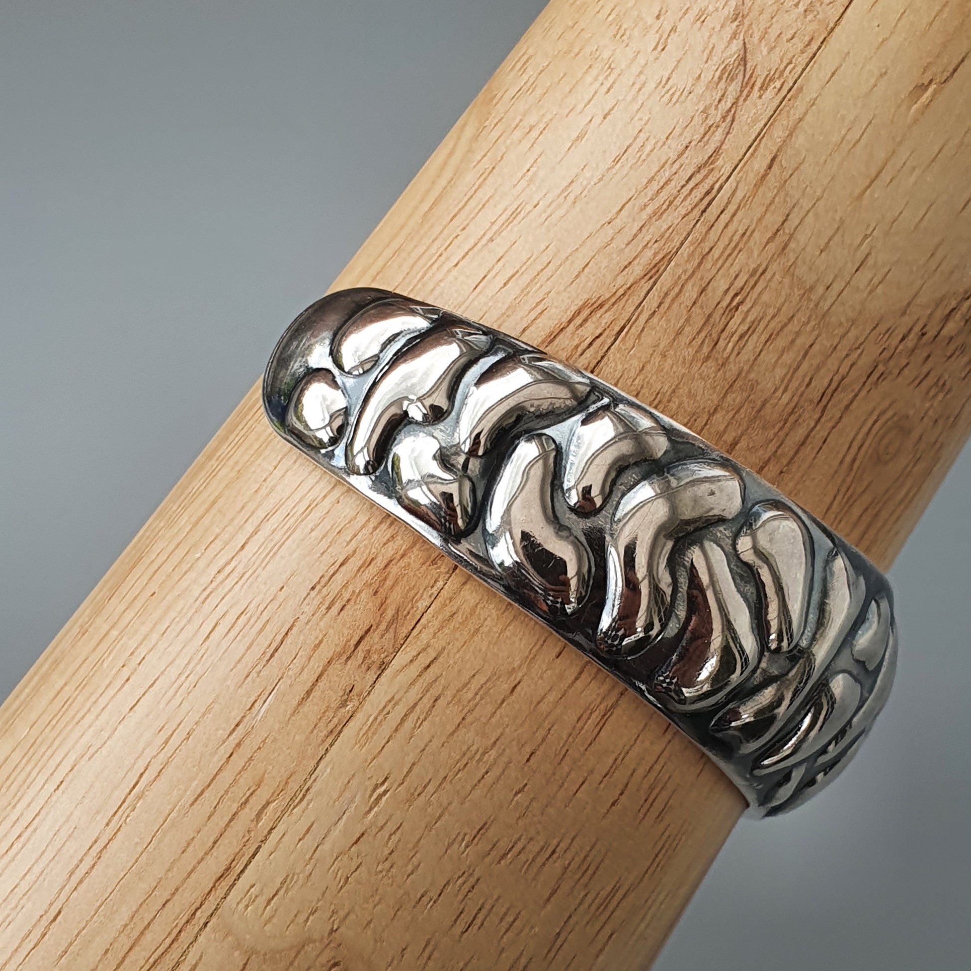 Silver ring with an intricate wavy or flame-like pattern engraved around its surface.