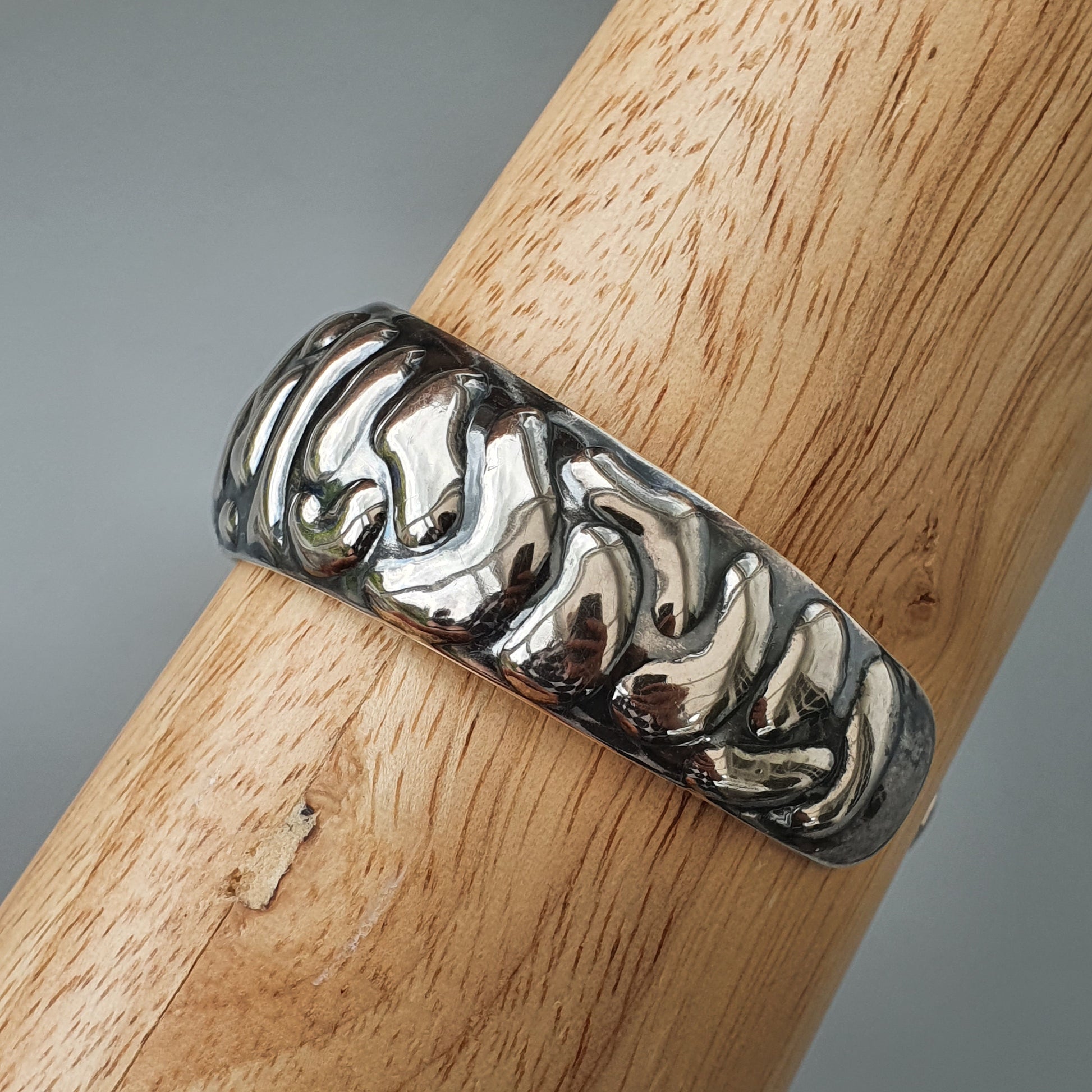 Silver ring with a wavy, textured pattern wrapped around a wooden surface.