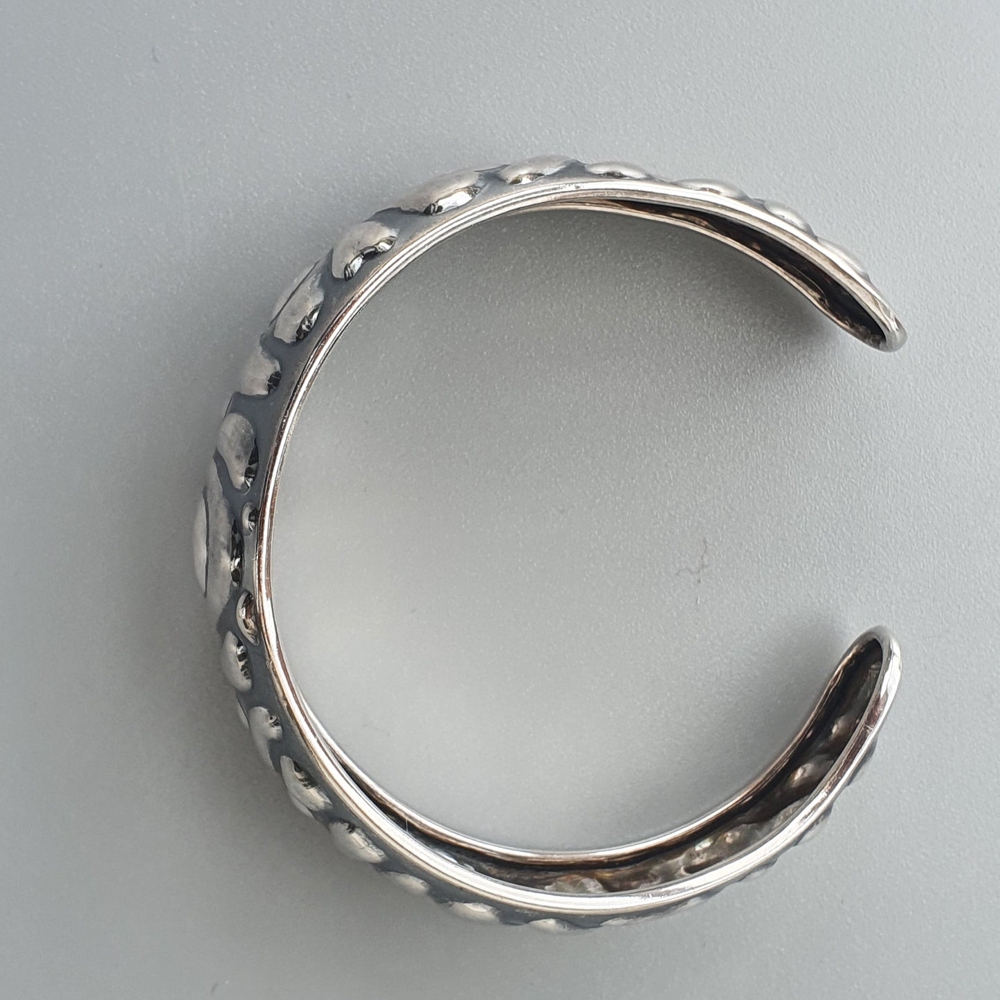 Silver cuff bracelet with a textured, bumpy surface design.