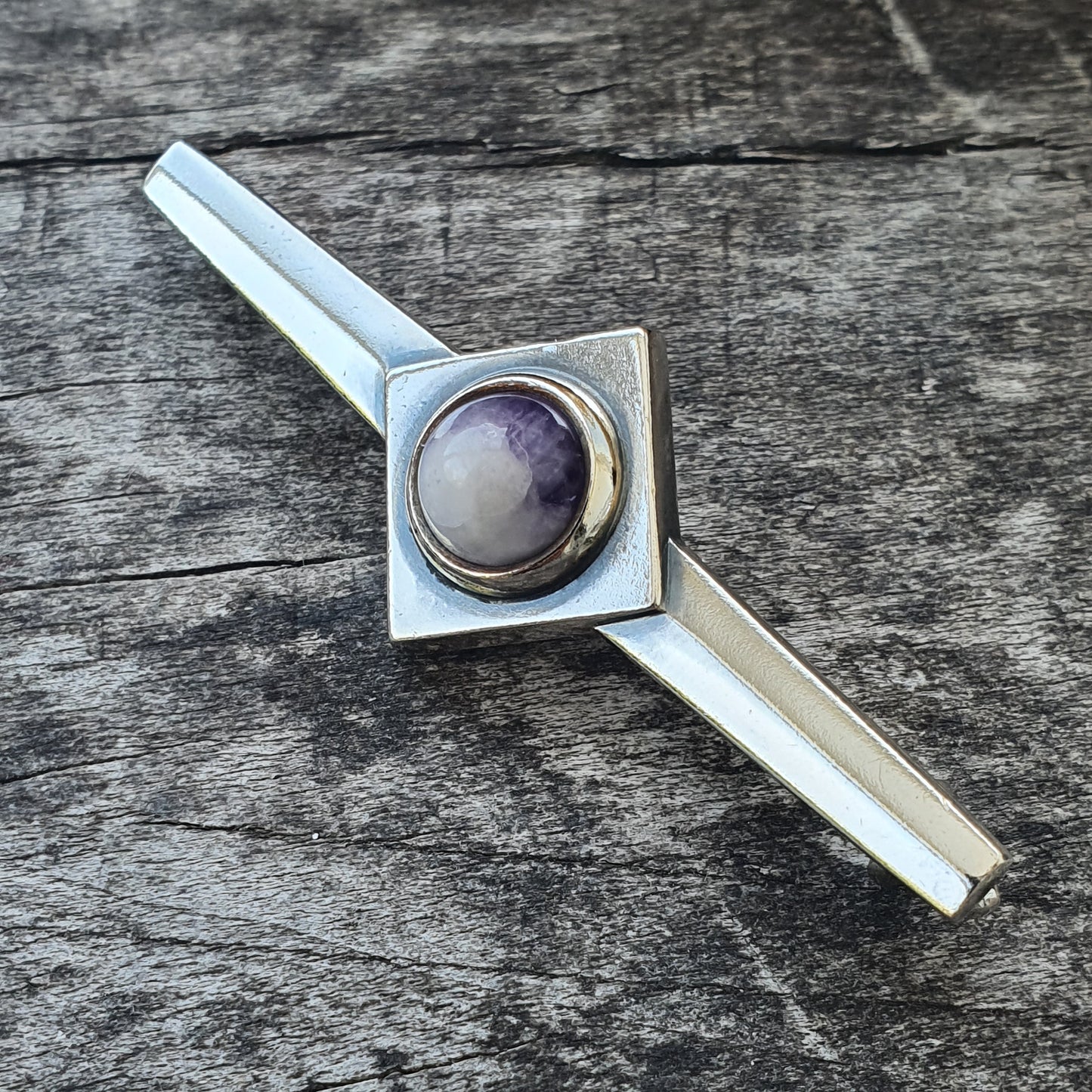 Silver tie clip featuring a diamond-shaped design with a round purple and white gemstone in the center.