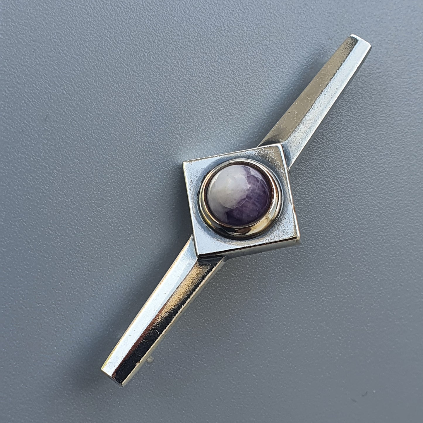 Metallic tie clip featuring a square setting with a purple gemstone.