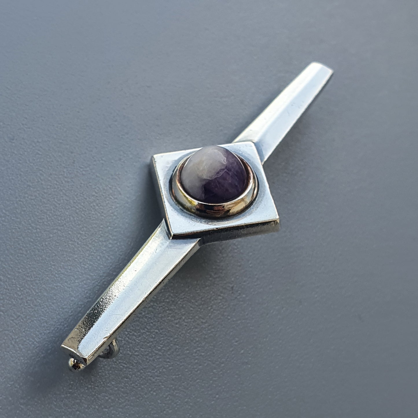 Sleek silver tie clip featuring a square base with a round purple gemstone.