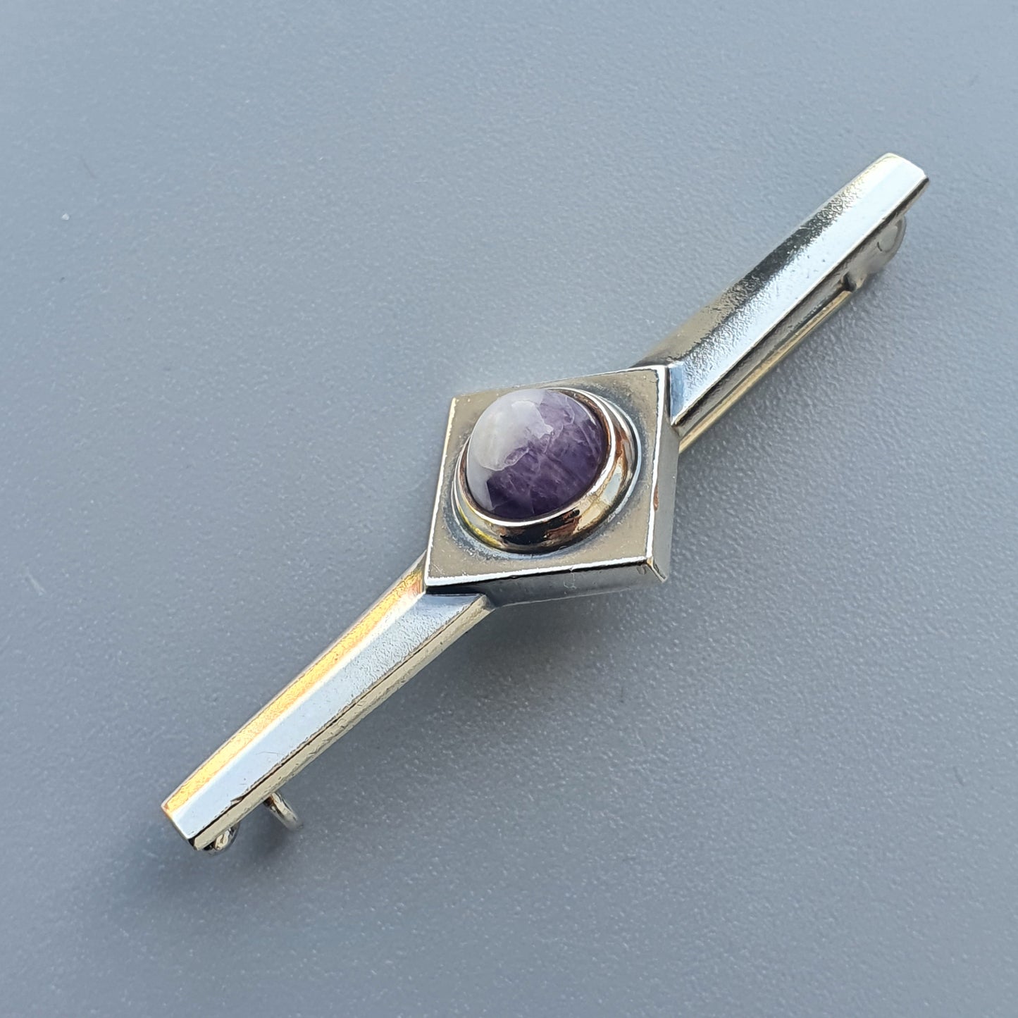 Silver tie clip featuring a purple gemstone set in a square design.