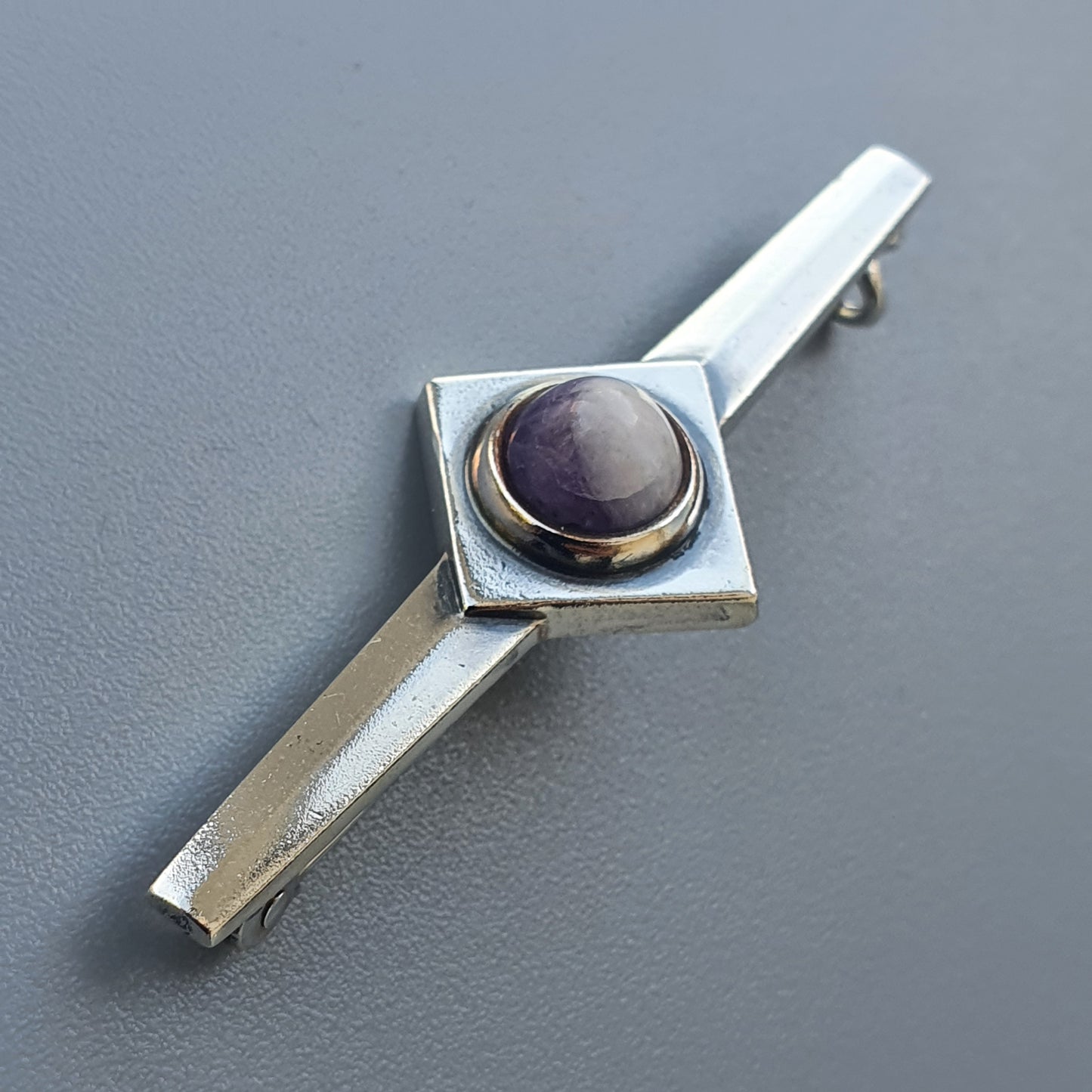 Silver tie clip featuring a square setting with a round purple gemstone.