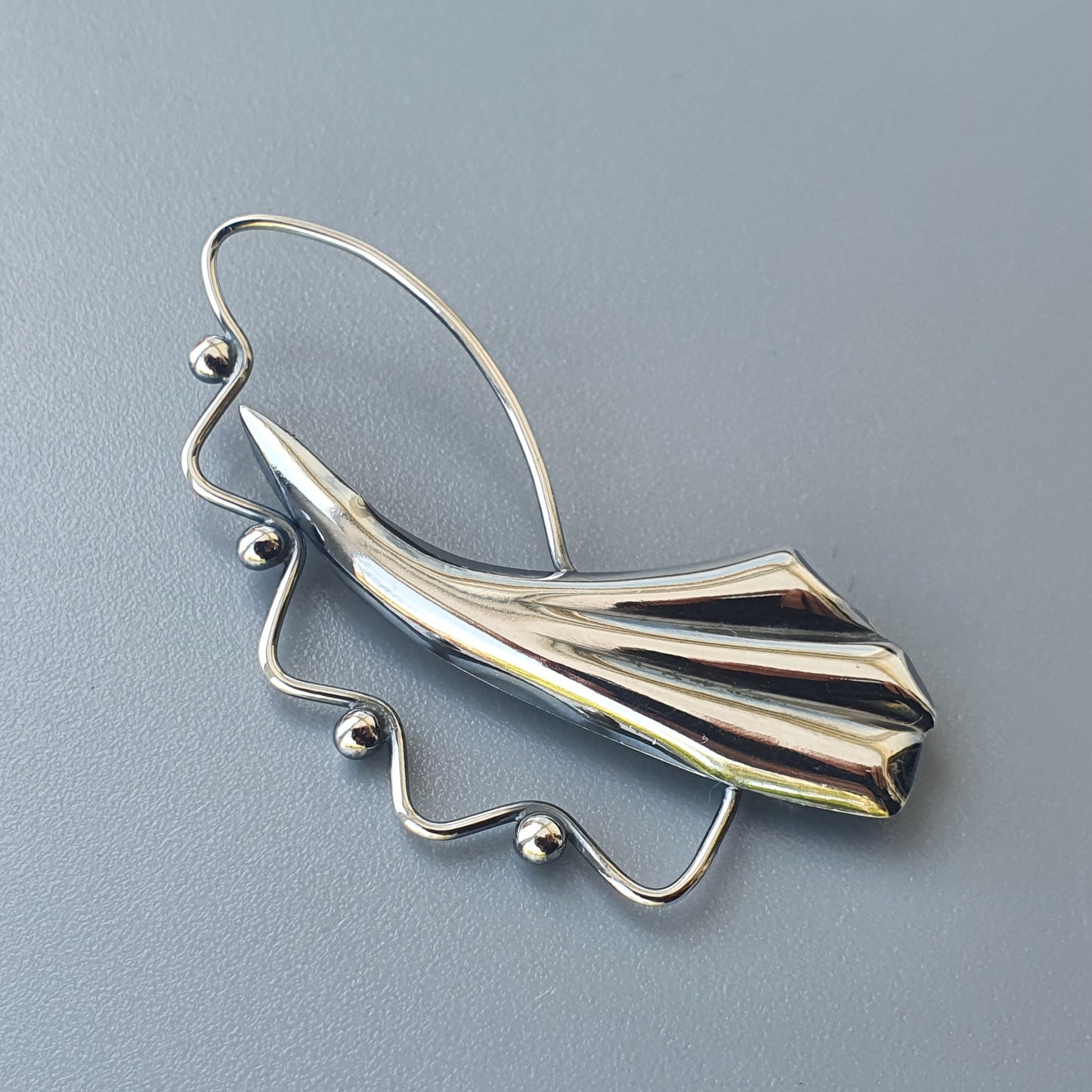 Stylized silver brooch or pendant shaped like an abstract wing or fan with beaded accents.