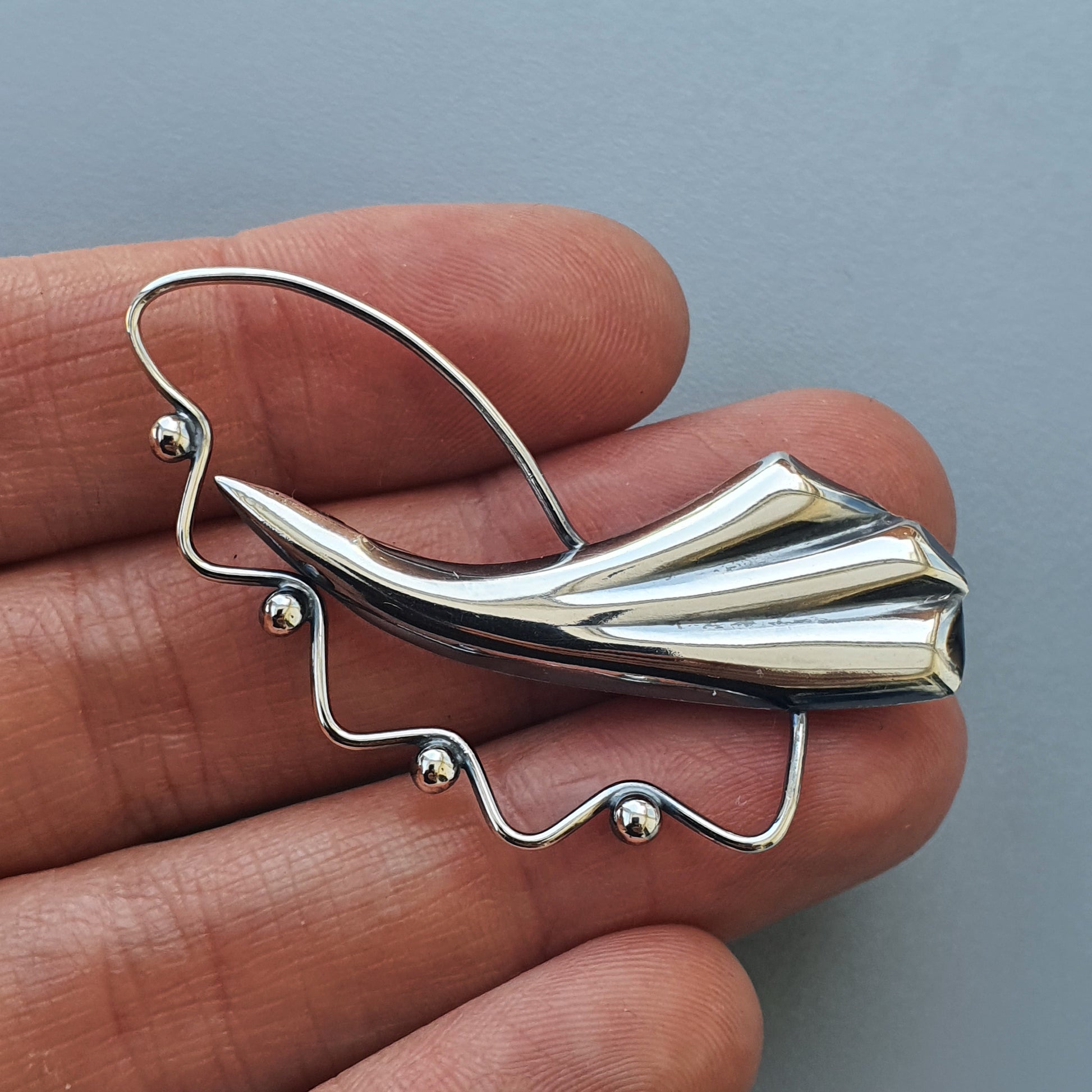 Silver brooch or pin shaped like an abstract bird or fish with flowing lines and small bead accents.