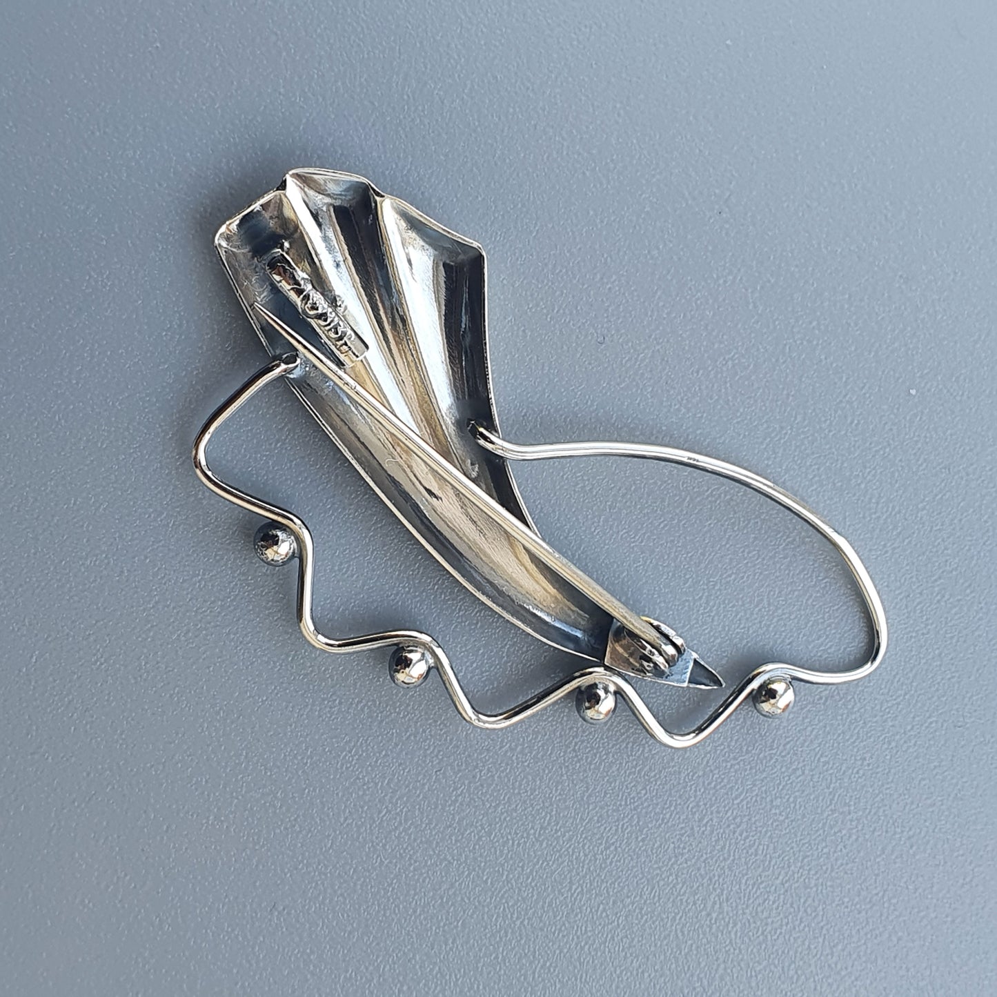 Silver brooch or pin shaped like a stylized leaf or petal with a curving stem.