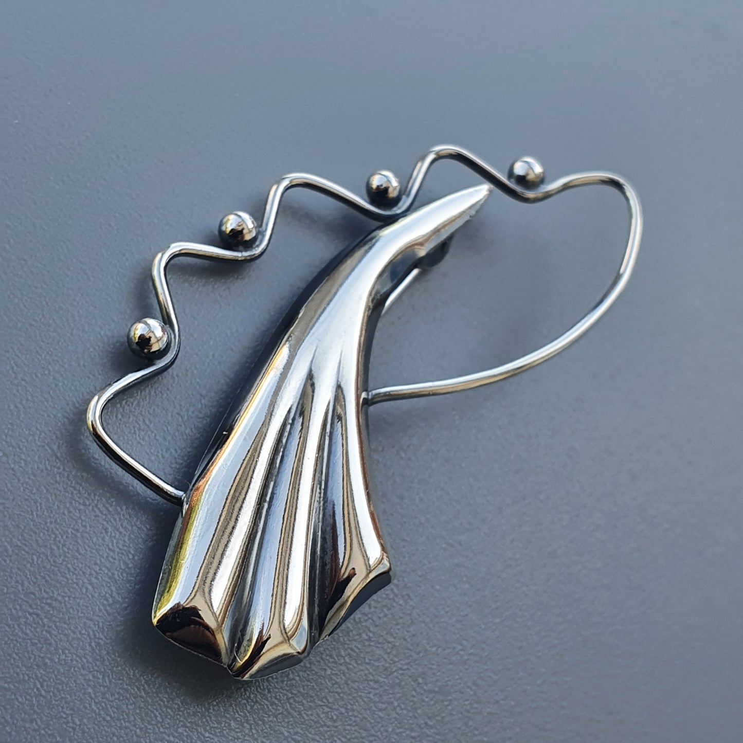 Stylized silver brooch or pendant shaped like an abstract wing or feather with a curved wire frame.