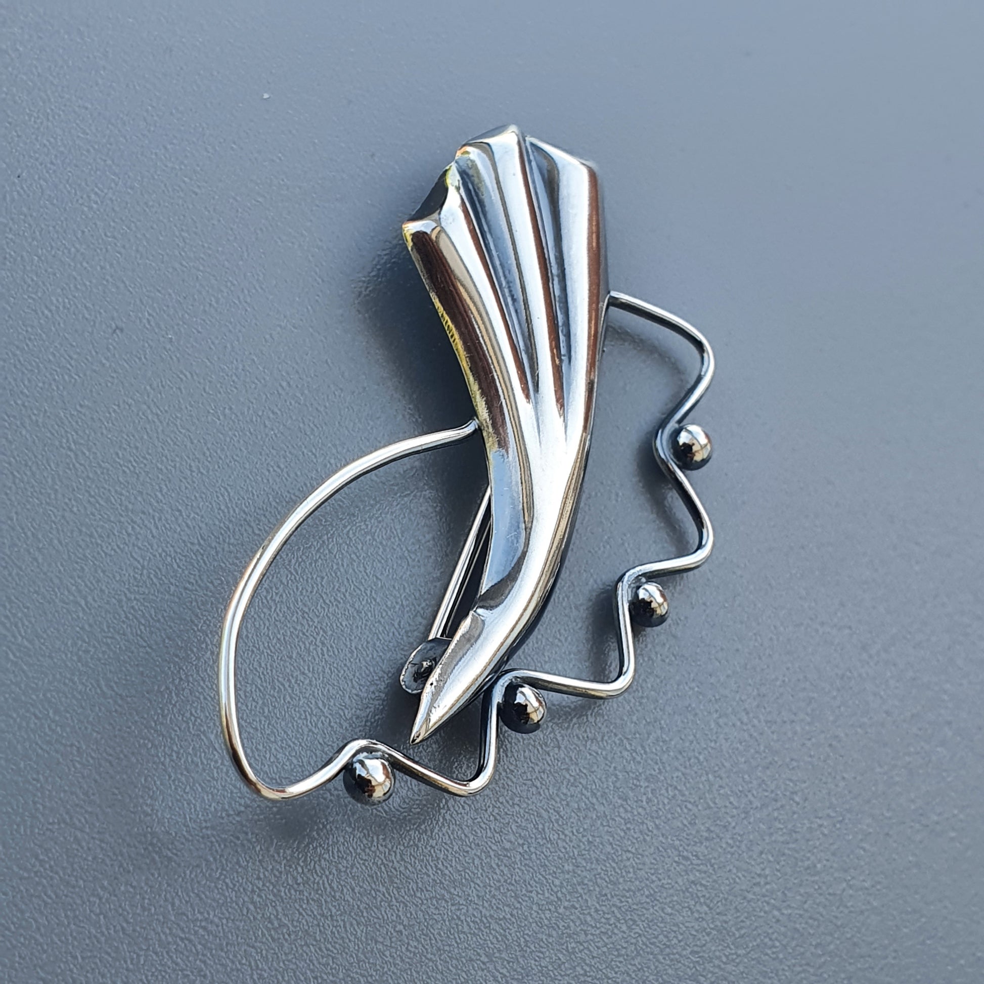 Stylized silver brooch or pin with an abstract wing-like design and curved wire elements.