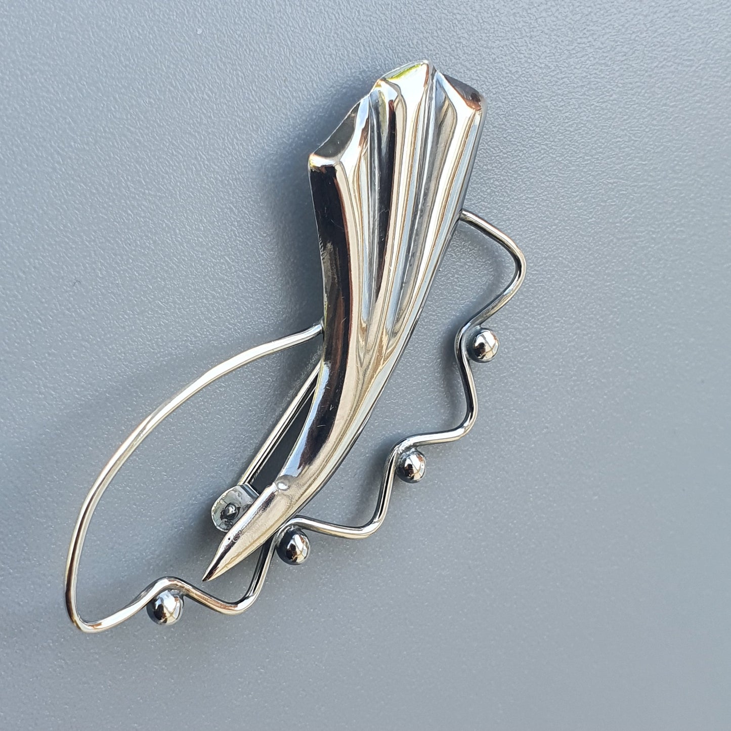 Silver brooch or pin with an abstract, elongated design featuring curved lines and small spherical accents.