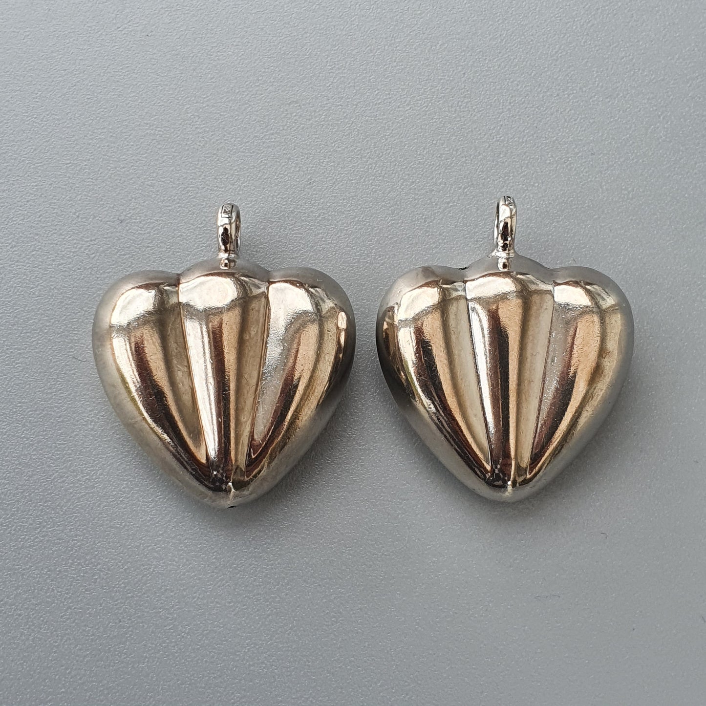 Two shiny silver heart-shaped pendants or charms.