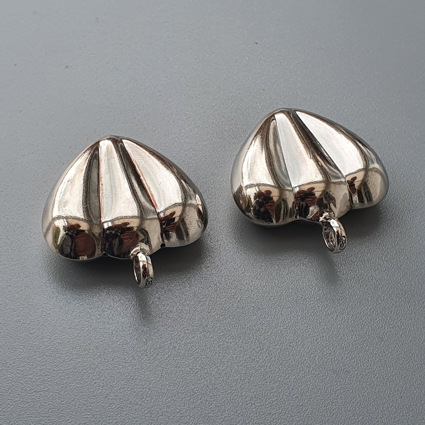 Pair of silver-colored, umbrella-shaped earrings or charms with ridged surfaces.