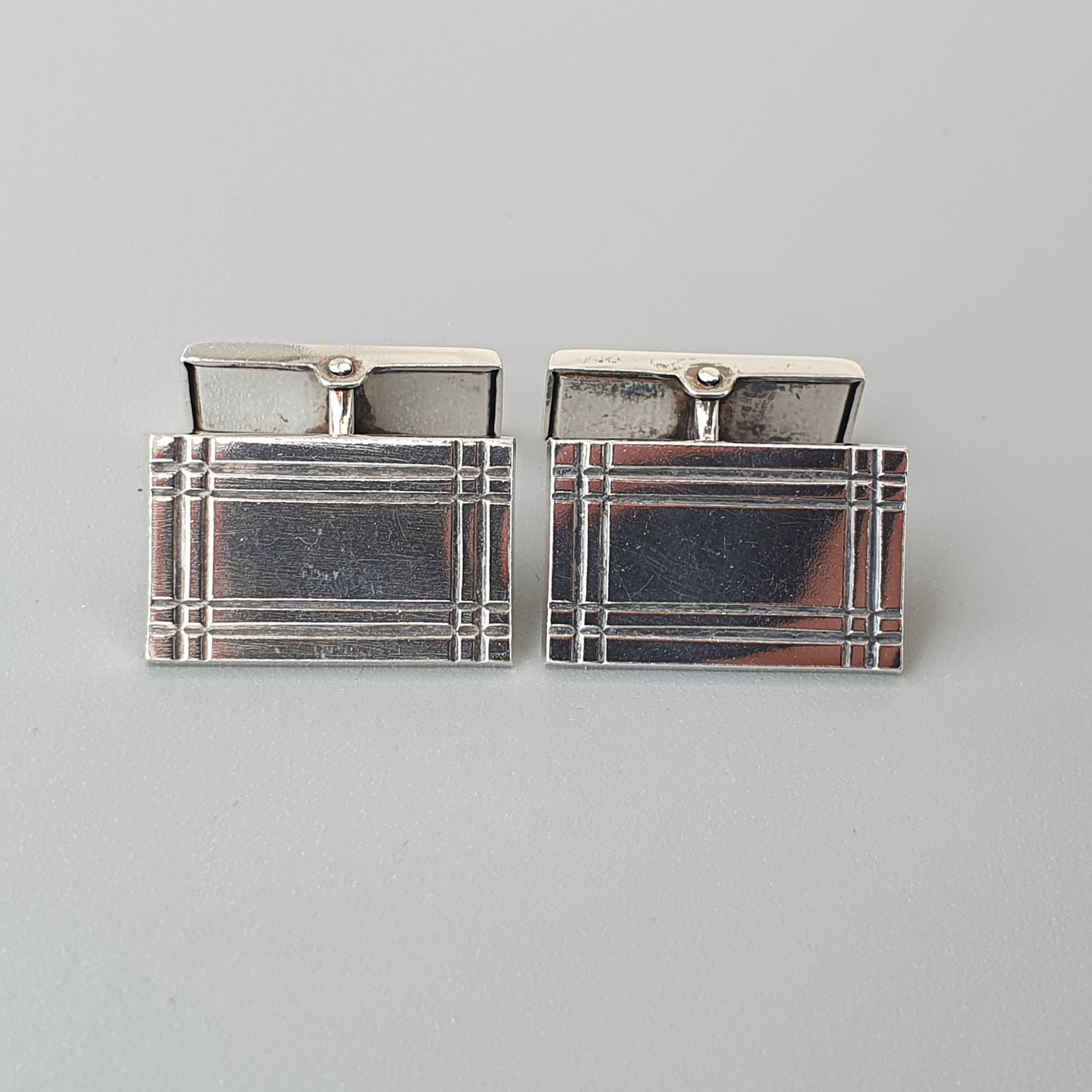 Pair of rectangular silver cufflinks with engraved linear patterns.