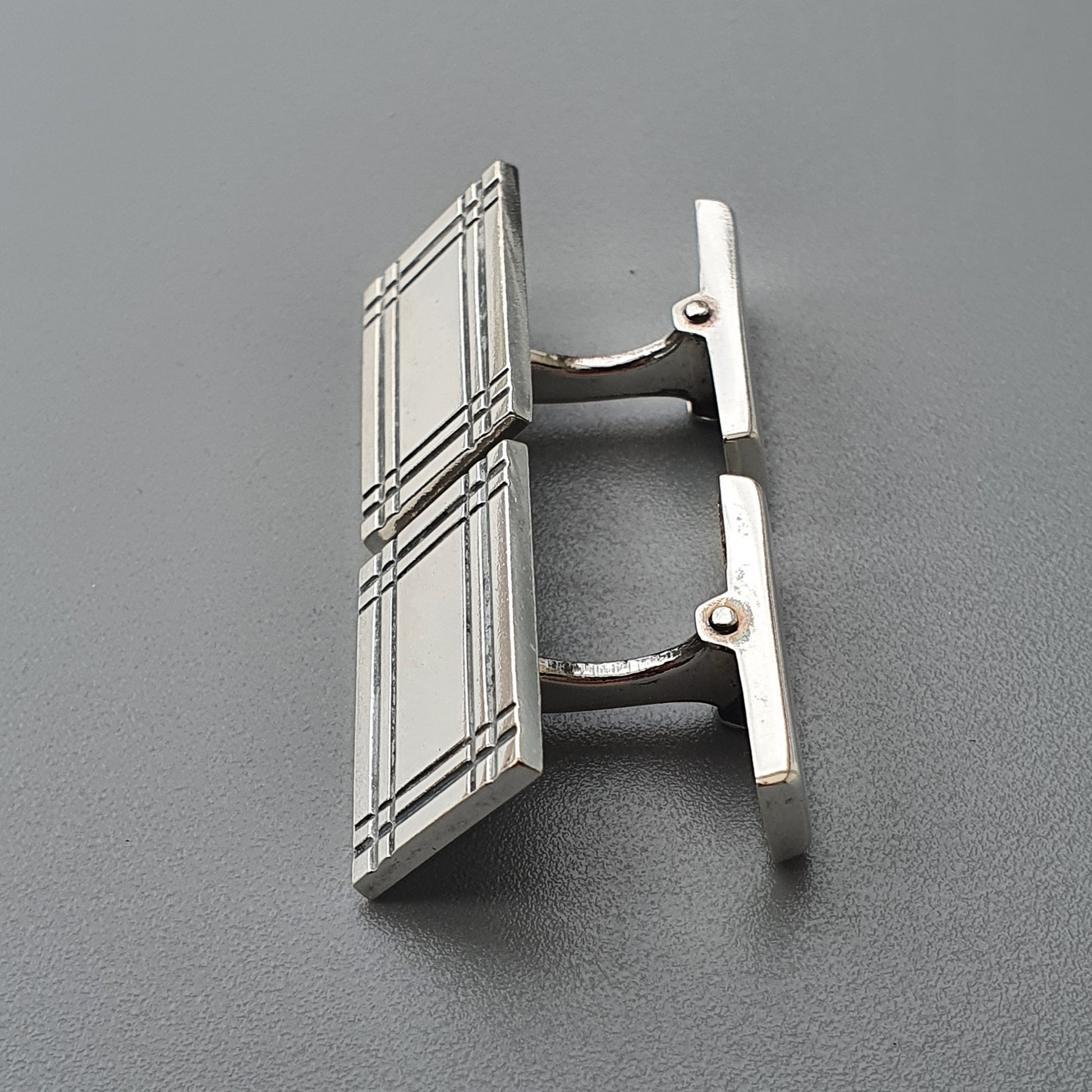 Silver cufflink with a geometric grid pattern on its rectangular face.