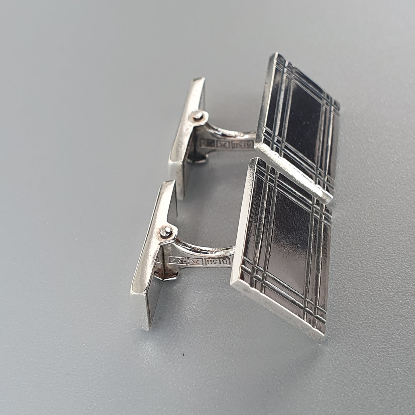 Pair of silver rectangular cufflinks with a geometric pattern.