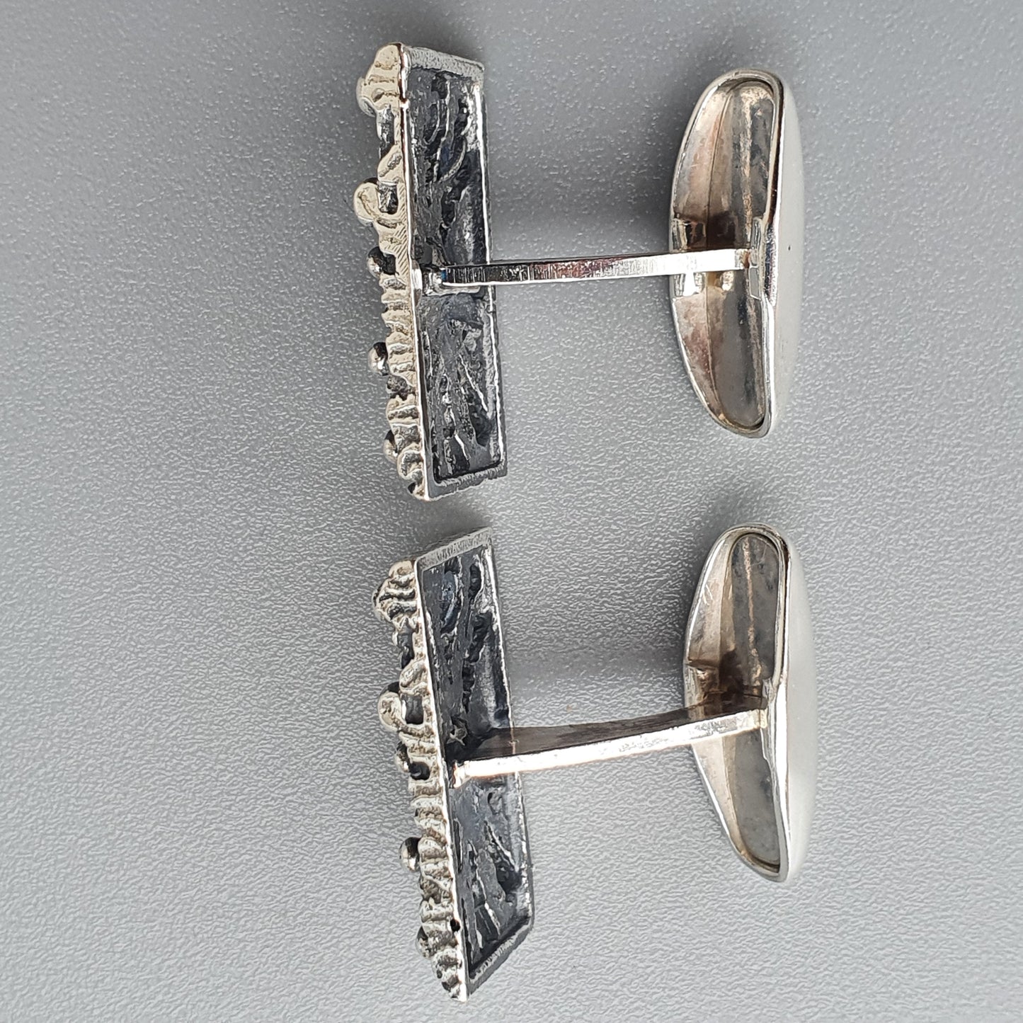 Pair of silver cufflinks with rectangular faces featuring intricate designs.