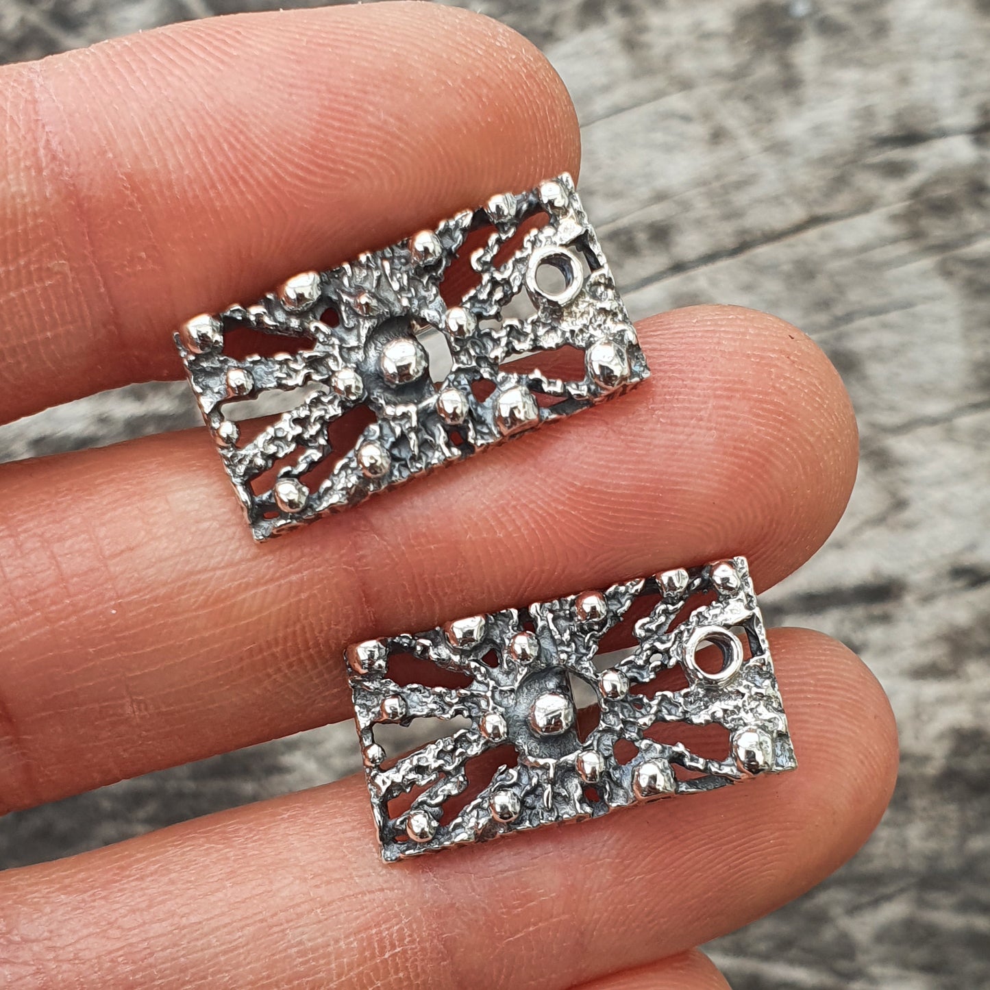 Pair of ornate silver rectangular jewelry pieces with intricate floral or starburst designs.