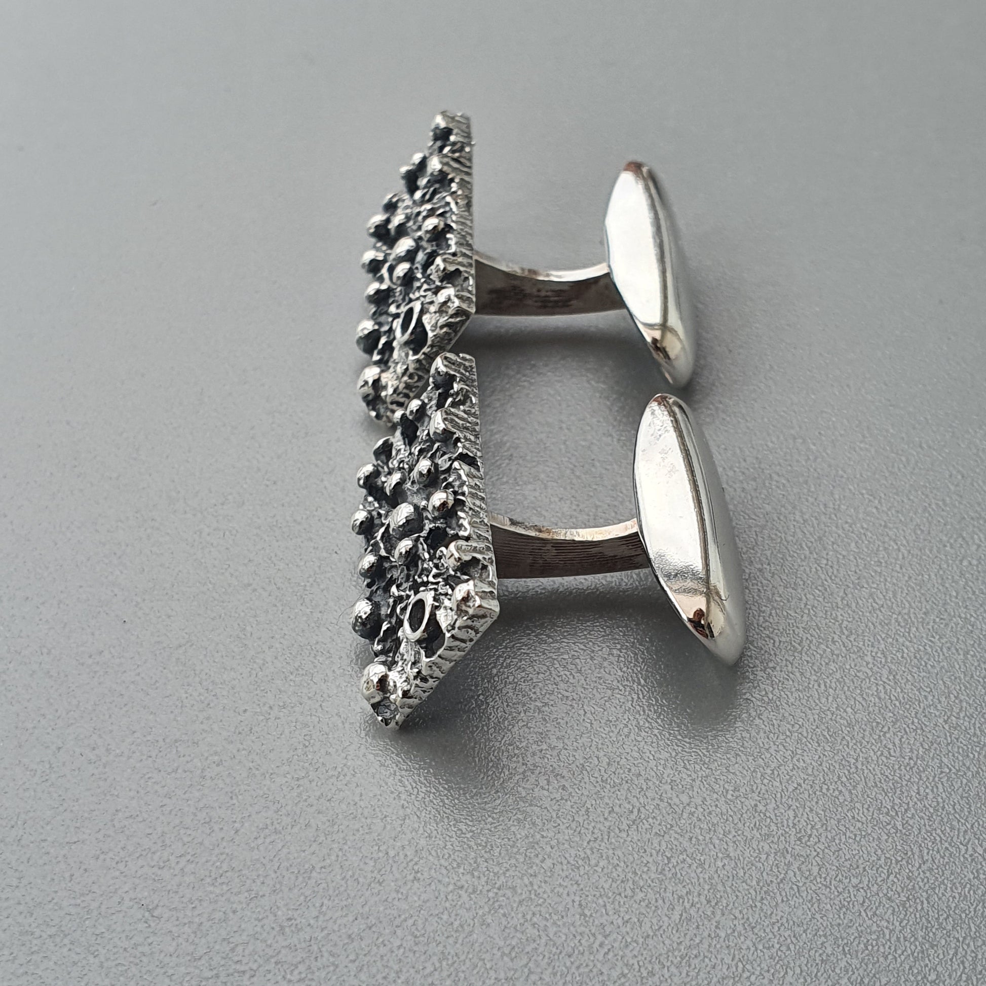 Pair of silver cufflinks with intricate textured designs on the front panels.