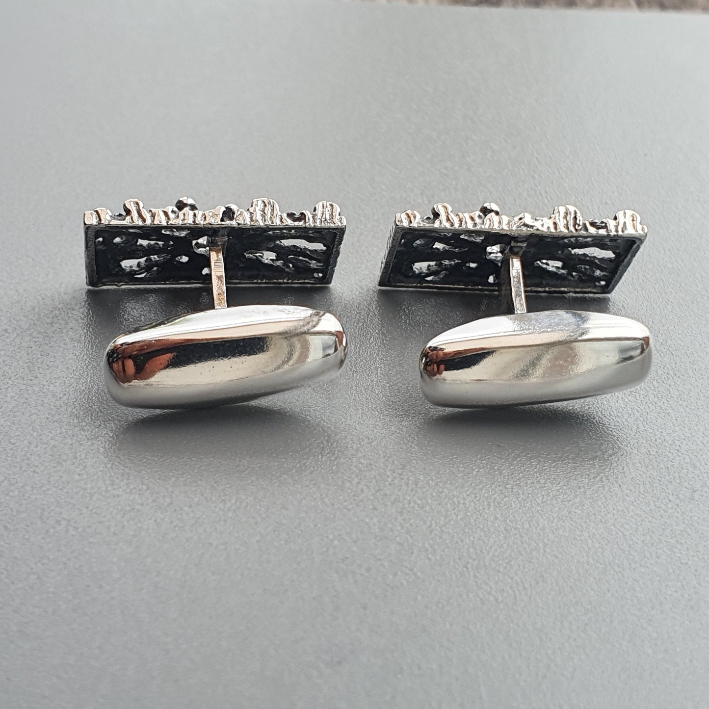 Pair of silver cufflinks with rectangular textured tops and oval smooth bottoms.