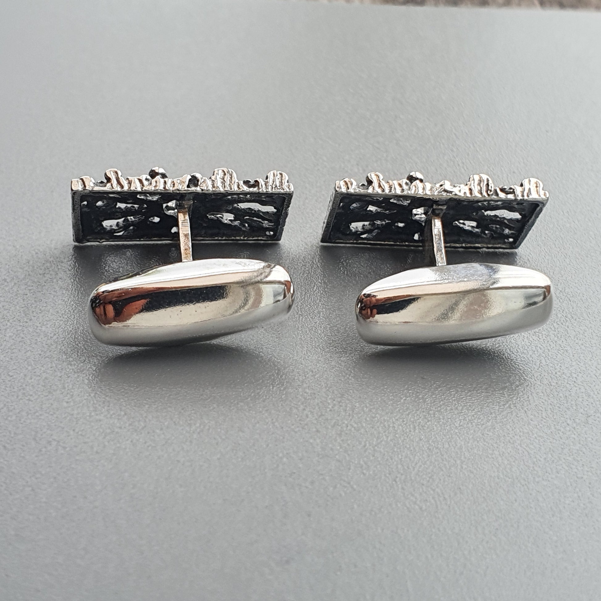 Pair of silver cufflinks with rectangular textured tops and oval smooth bottoms.