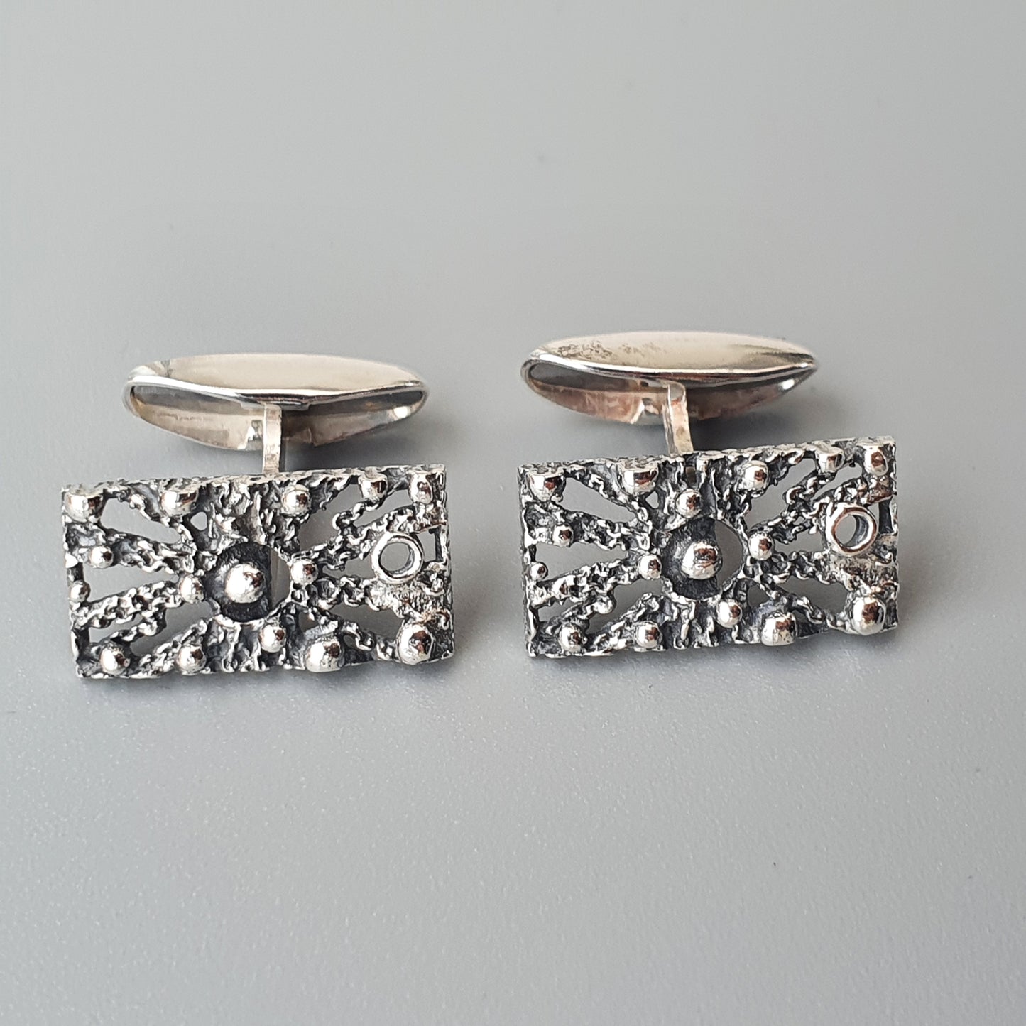 Pair of silver cufflinks with textured rectangular faces featuring a lunar-like surface design.