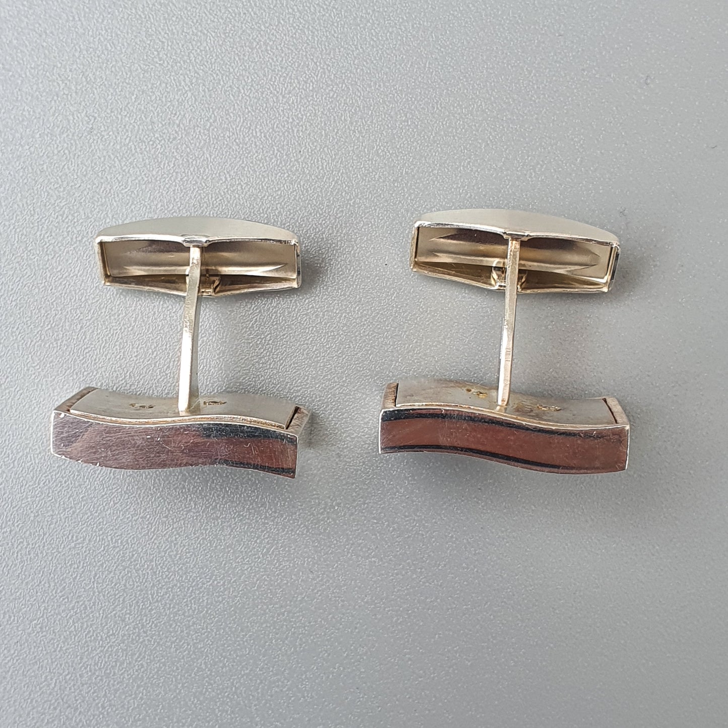 Pair of vintage cufflinks with rectangular gold tops and curved copper-colored bases.