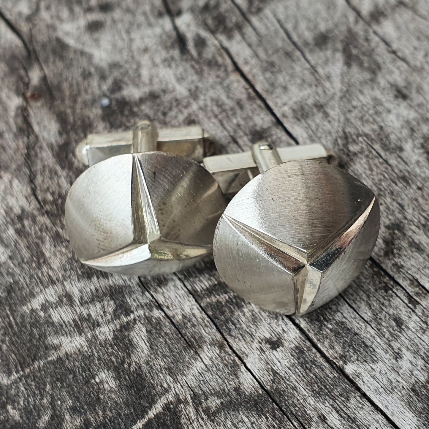 Pair of silver cufflinks with a triangular cut design.