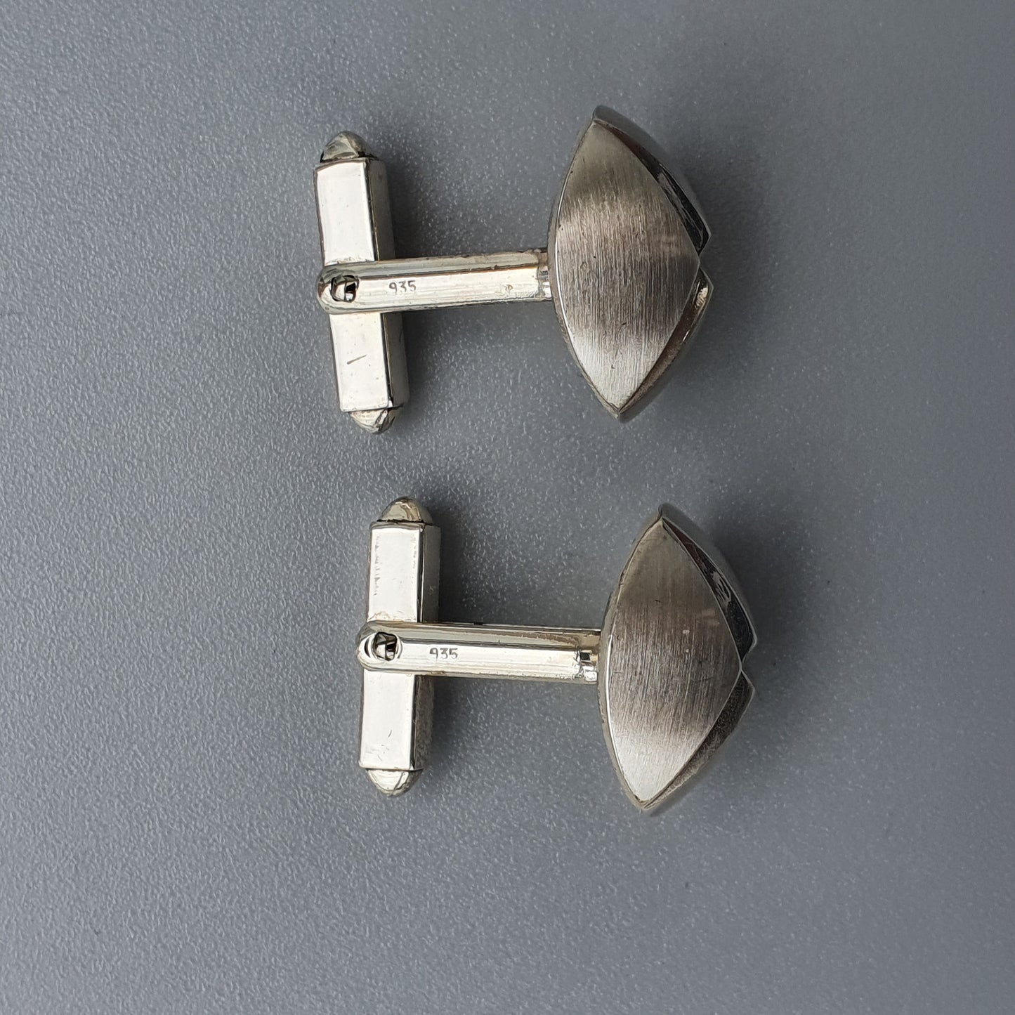 Pair of silver-toned metal cufflinks with curved shield-shaped faces.