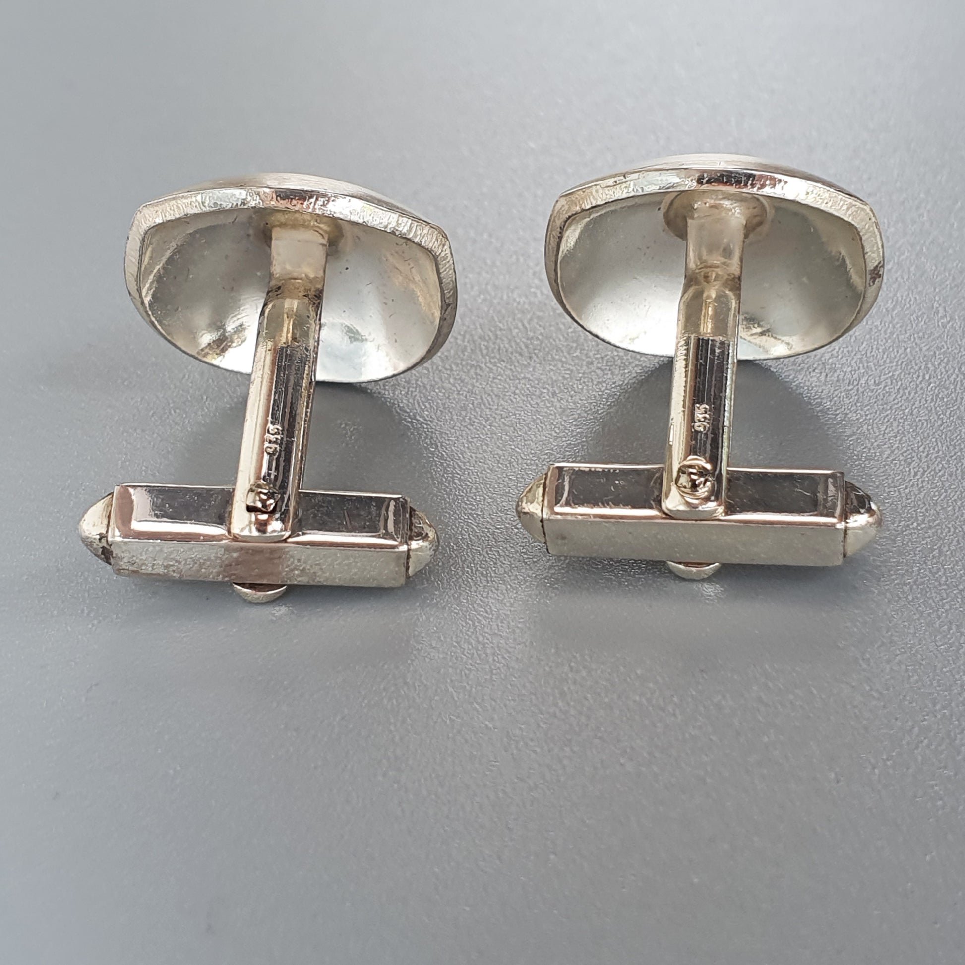 Pair of silver-colored oval cufflinks with bar-shaped fasteners.