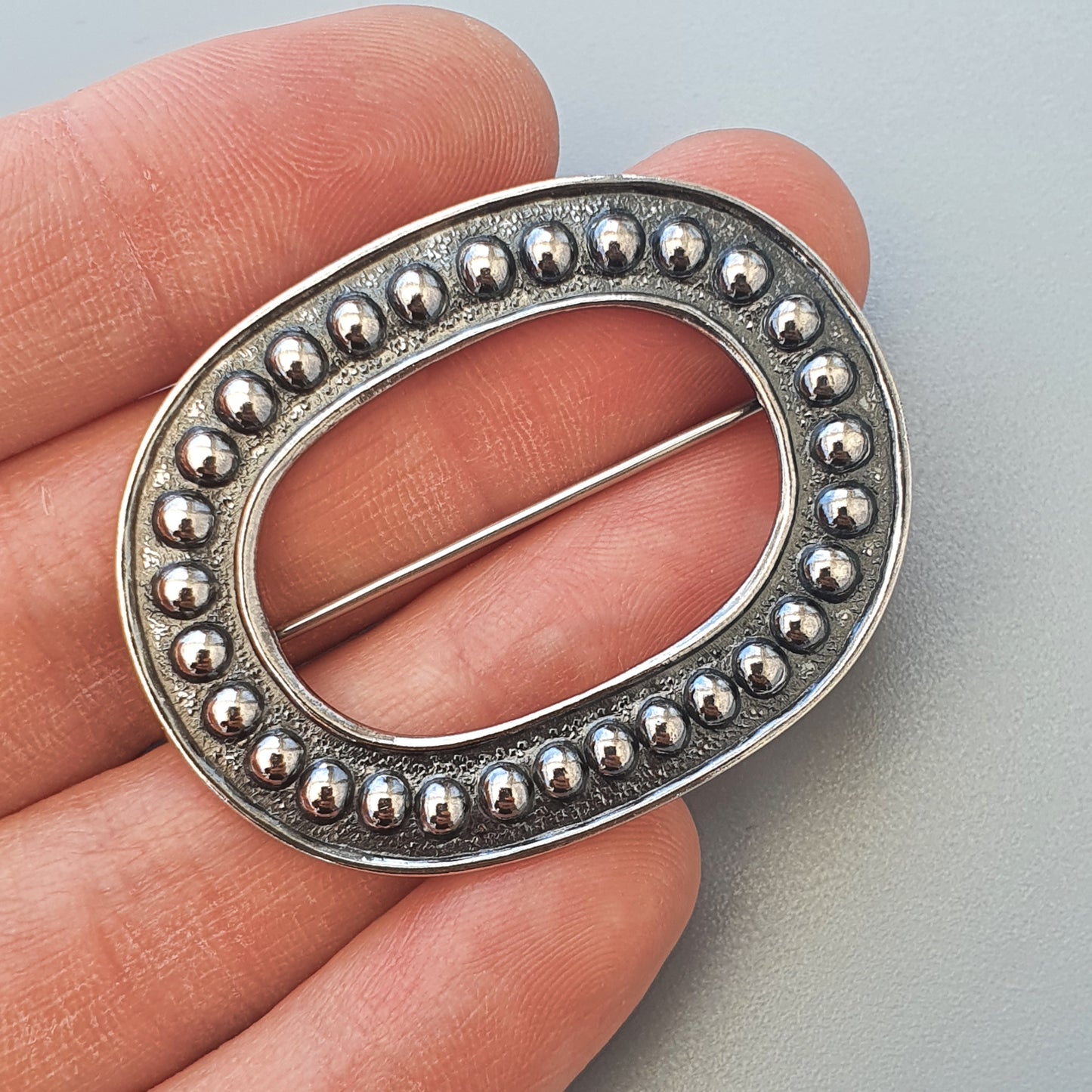 Oval-shaped metal brooch or buckle with beaded edge decoration.