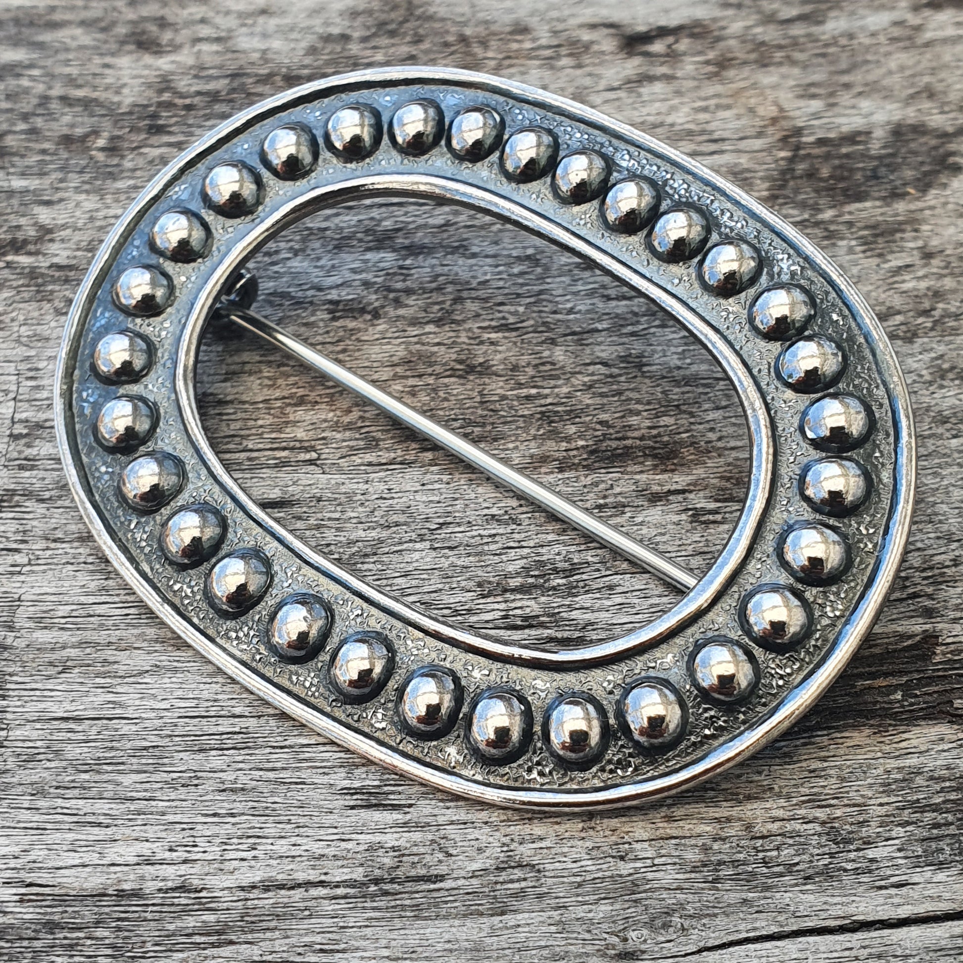 Oval silver brooch or pin with beaded edge design.