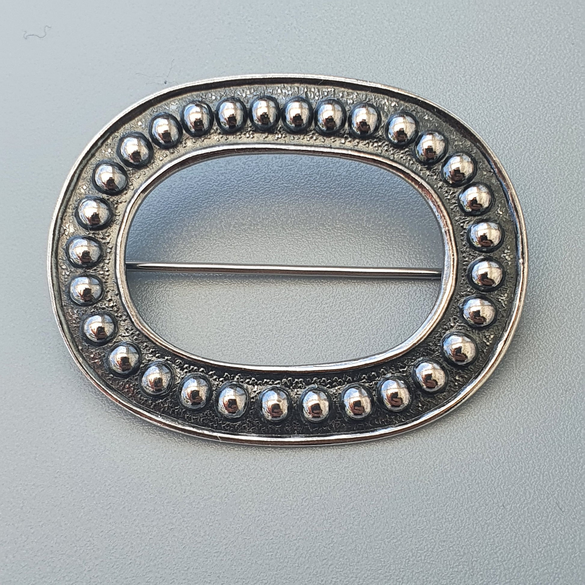 Oval silver brooch with beaded border design.