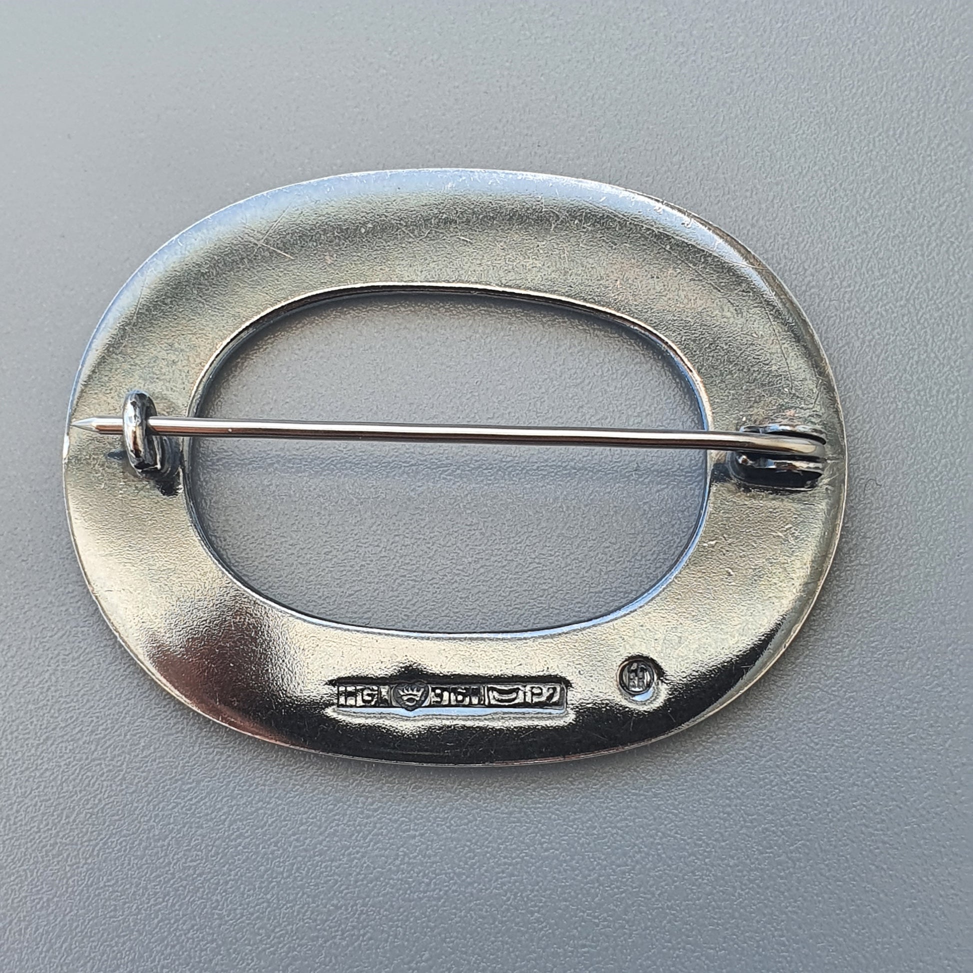 Oval-shaped silver brooch with a horizontal pin across its center.